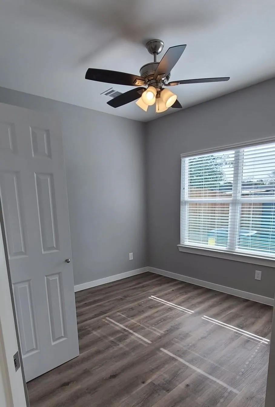Room featuring vinyl flooring, a ceiling fan with integrated lighting, a window with horizontal blinds, and a white interior door