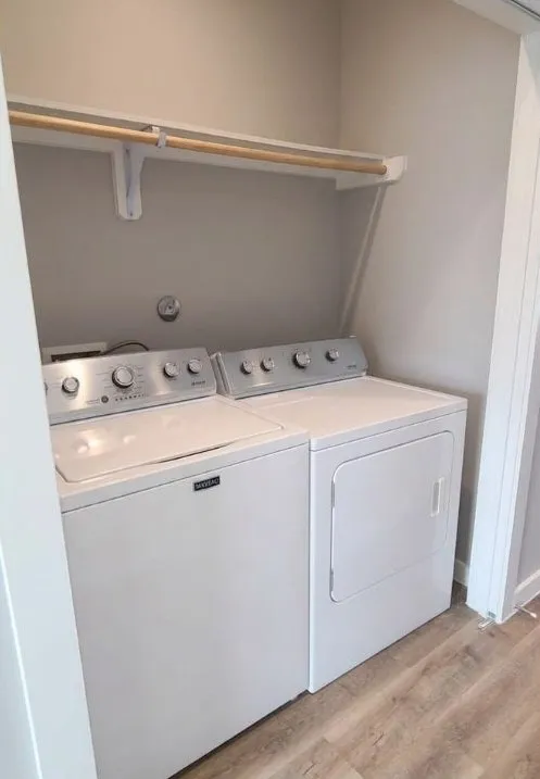 Dedicated laundry area with a top-load washing machine, front-load dryer, built-in shelving, and wood-finish flooring