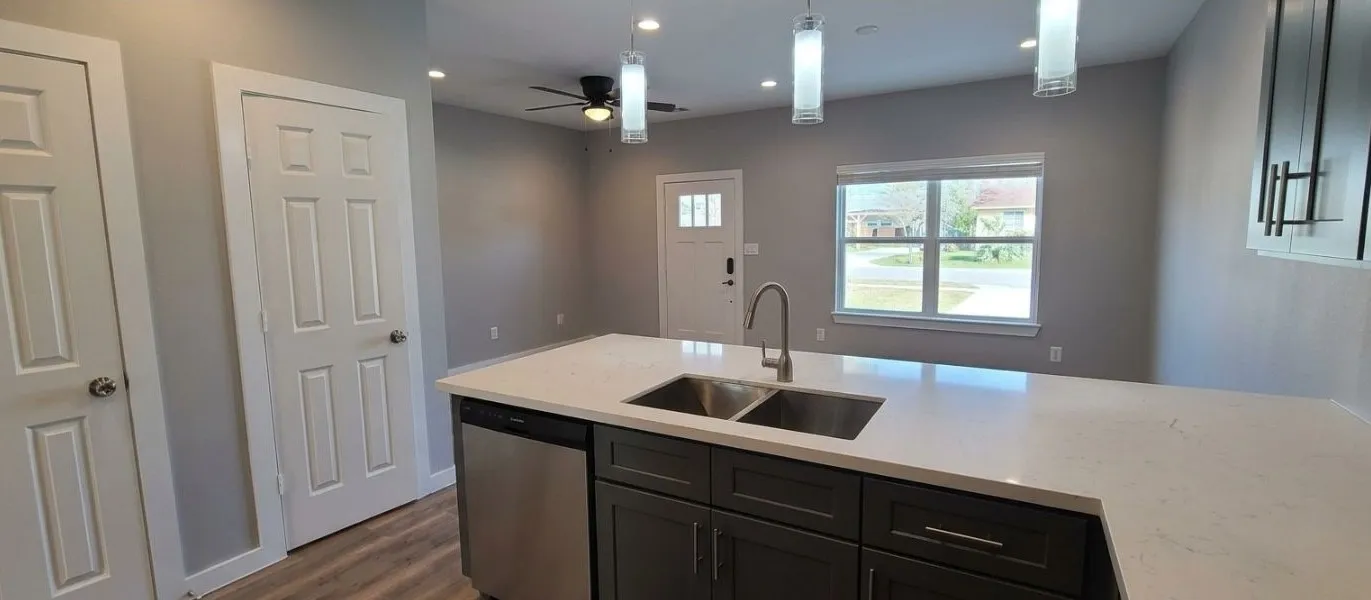 Kitchen island featuring a double basin stainless steel sink, a stainless steel dishwasher, and a light-toned countertop
