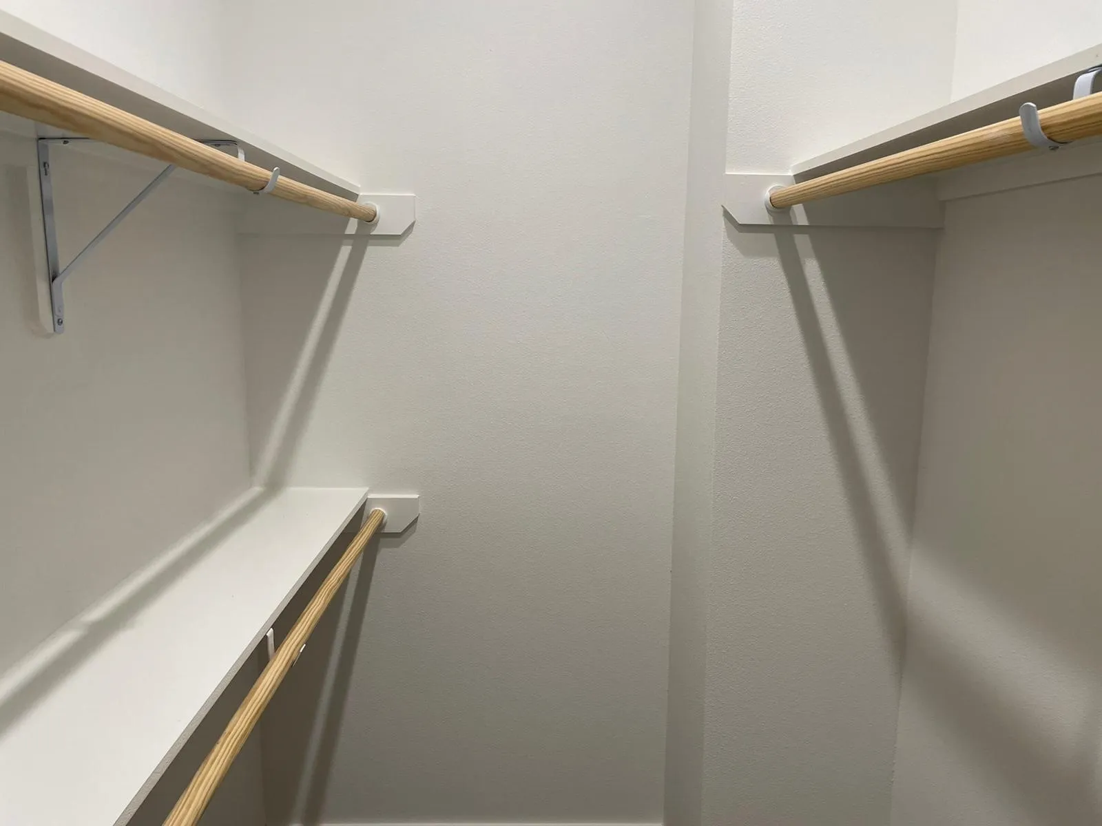 Walk-in closet featuring white painted walls, white shelving, and natural wood clothing rods