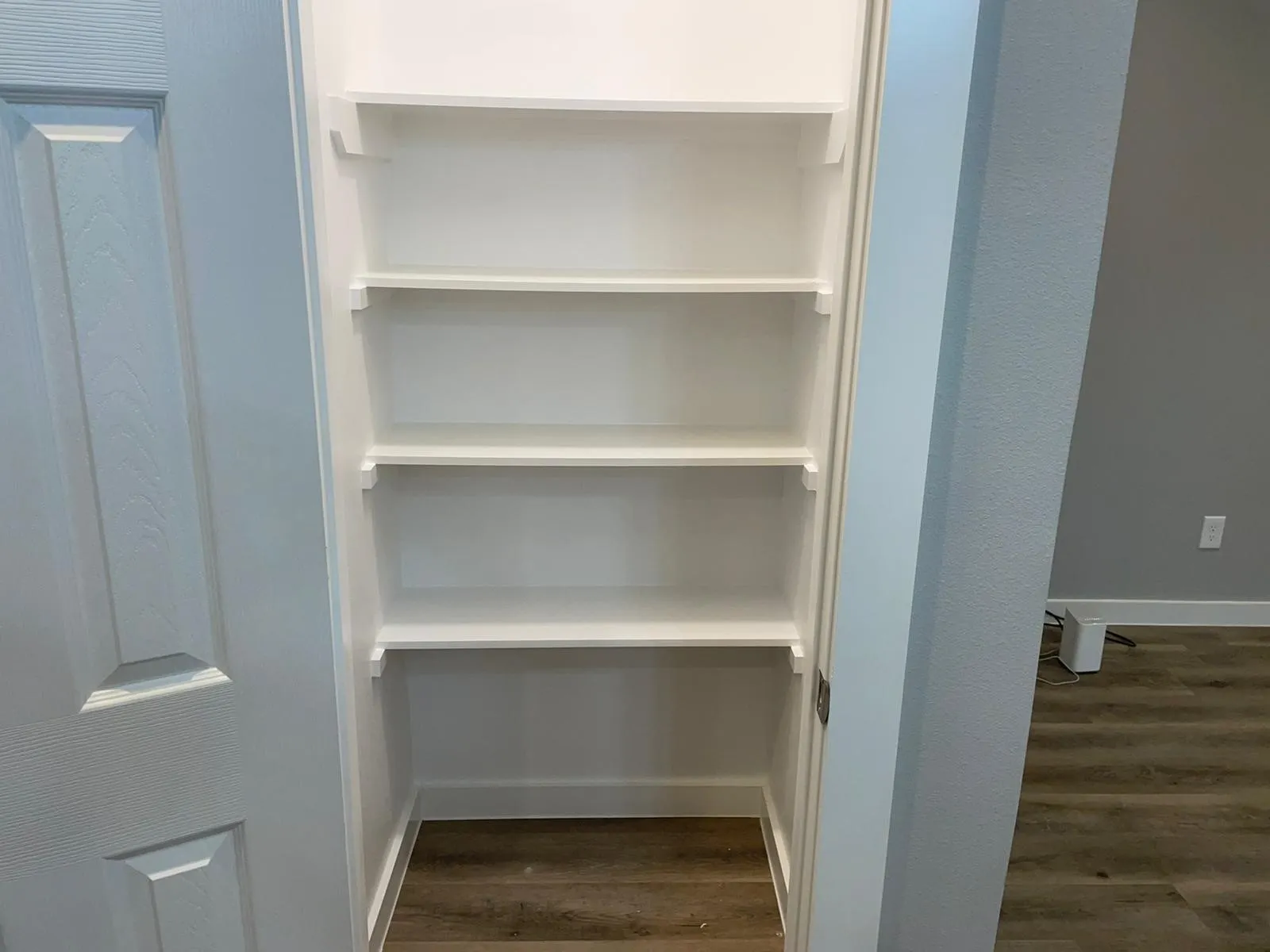Kitchen Pantry with Built-in shelving unit with five white shelves, white baseboard, and wood-finish flooring