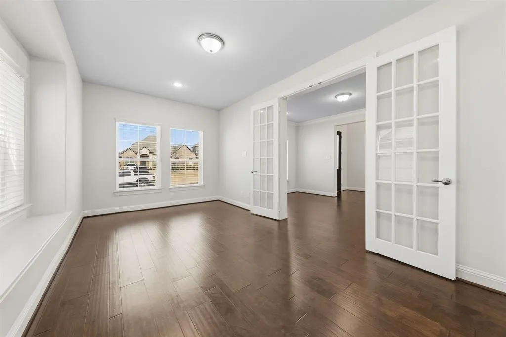 Spacious interior room featuring rich wood-finish flooring, white trim, and two large windows with blinds