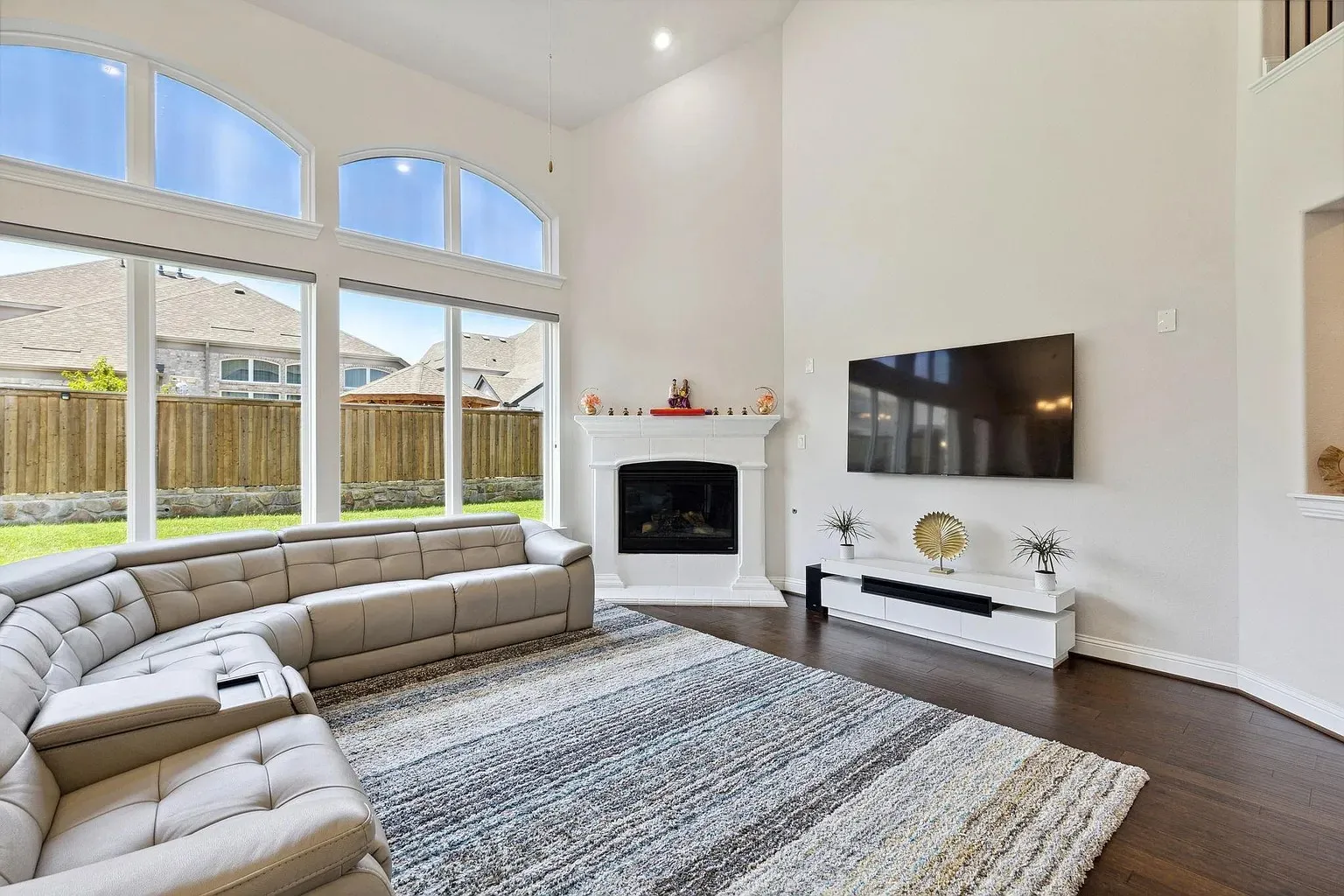 Two-story living area featuring a white mantel fireplace, dark wood-finish flooring, and a wall of windows with arched transom elements