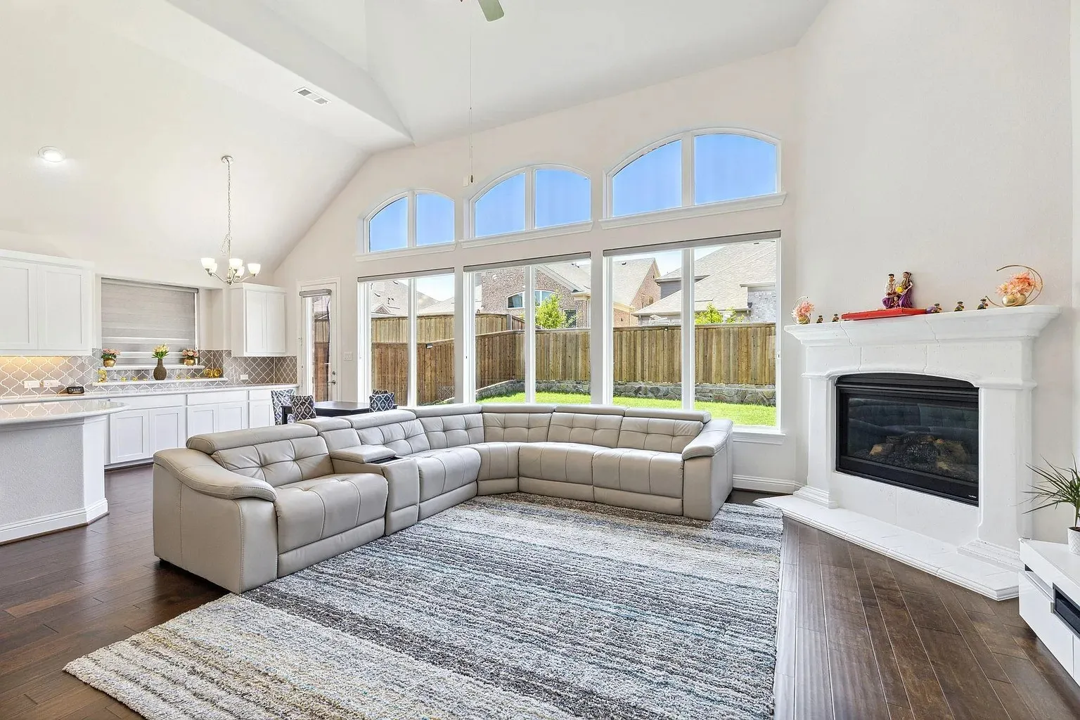 Spacious living area featuring high vaulted ceilings, expansive windows, a white mantel fireplace, and dark wood-finish flooring