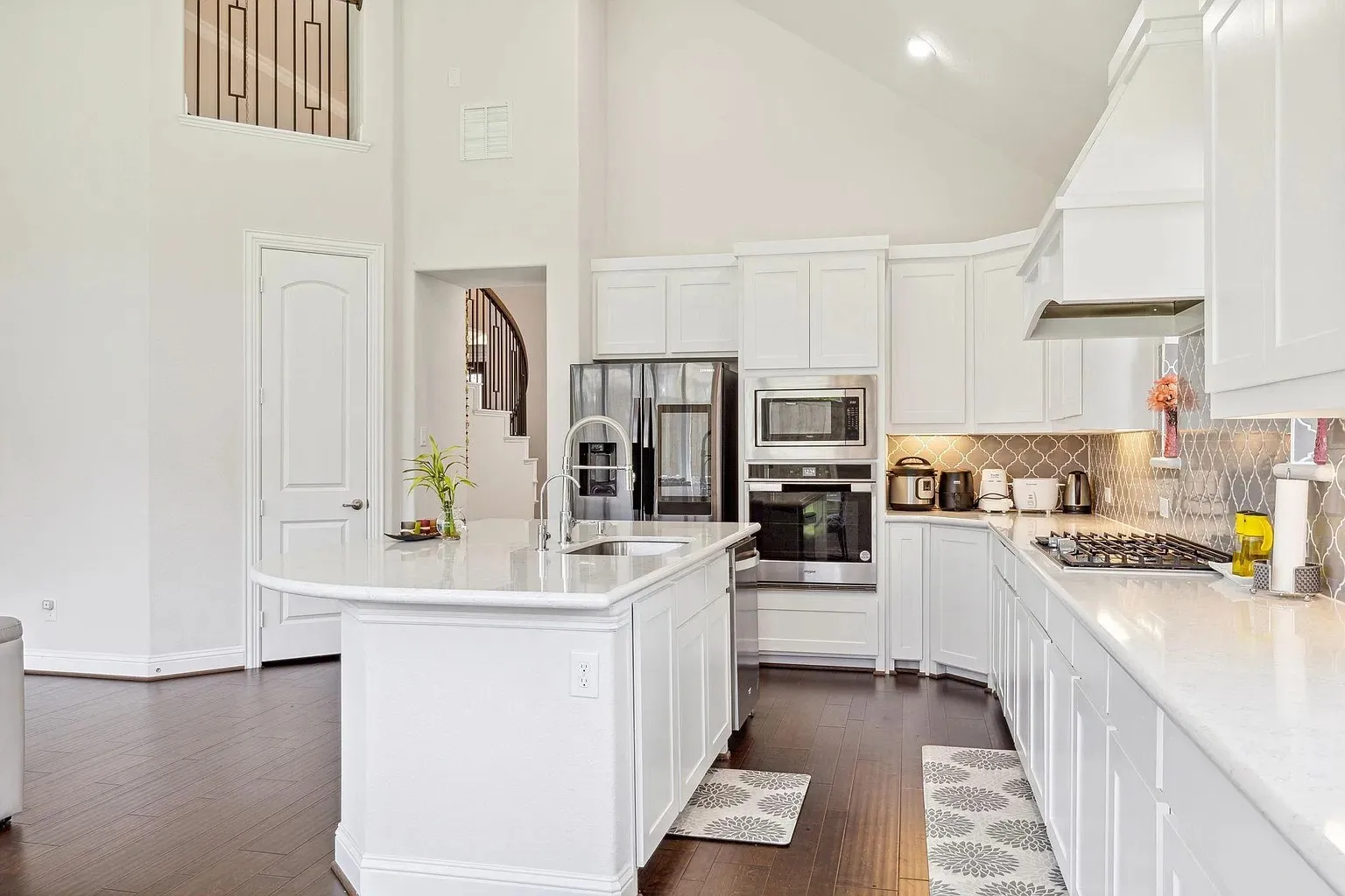 Kitchen with white cabinetry, stainless steel appliances, and a curved island featuring a sink