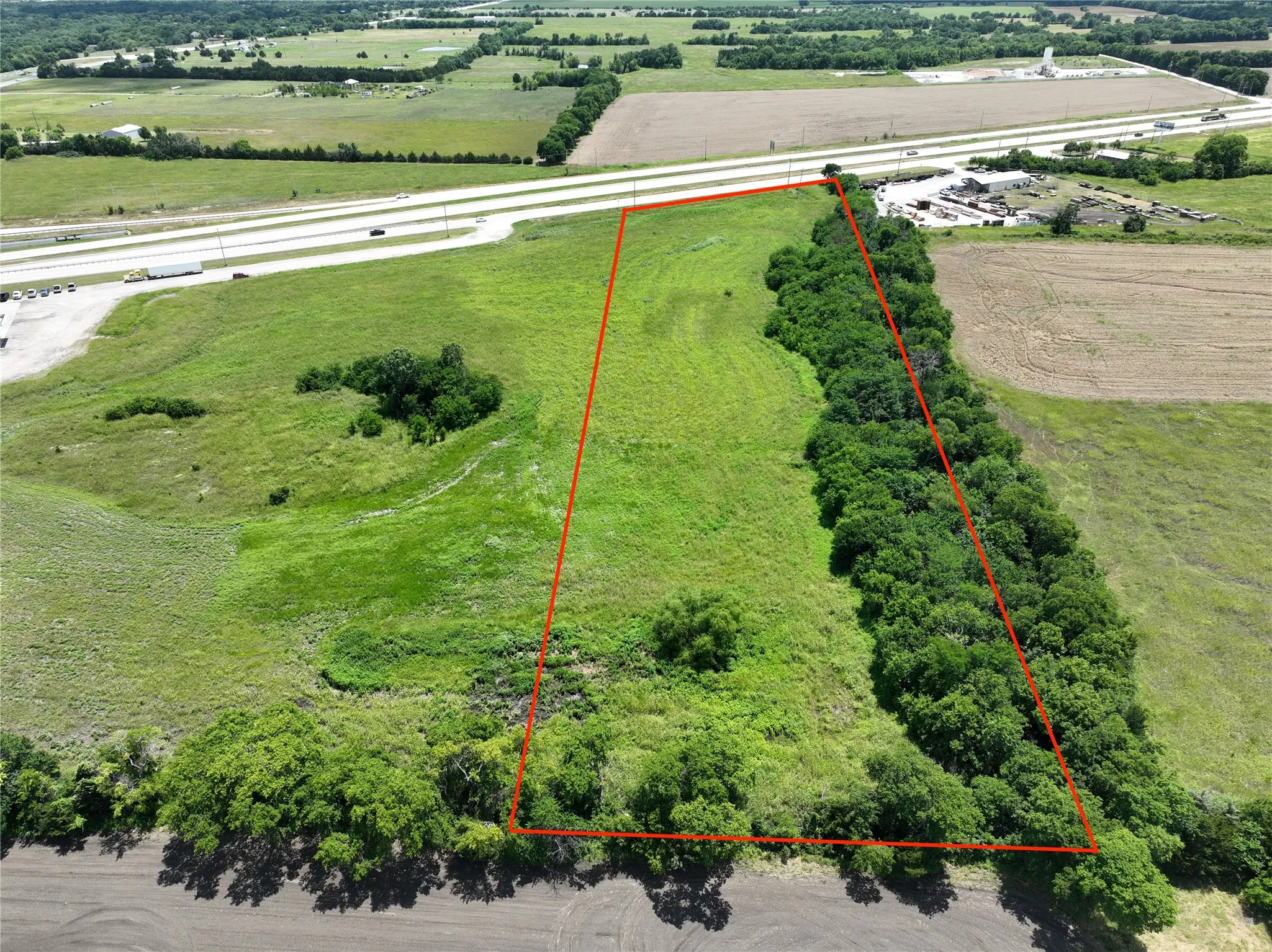 Expansive undeveloped land featuring a perimeter of mature trees and direct highway frontage