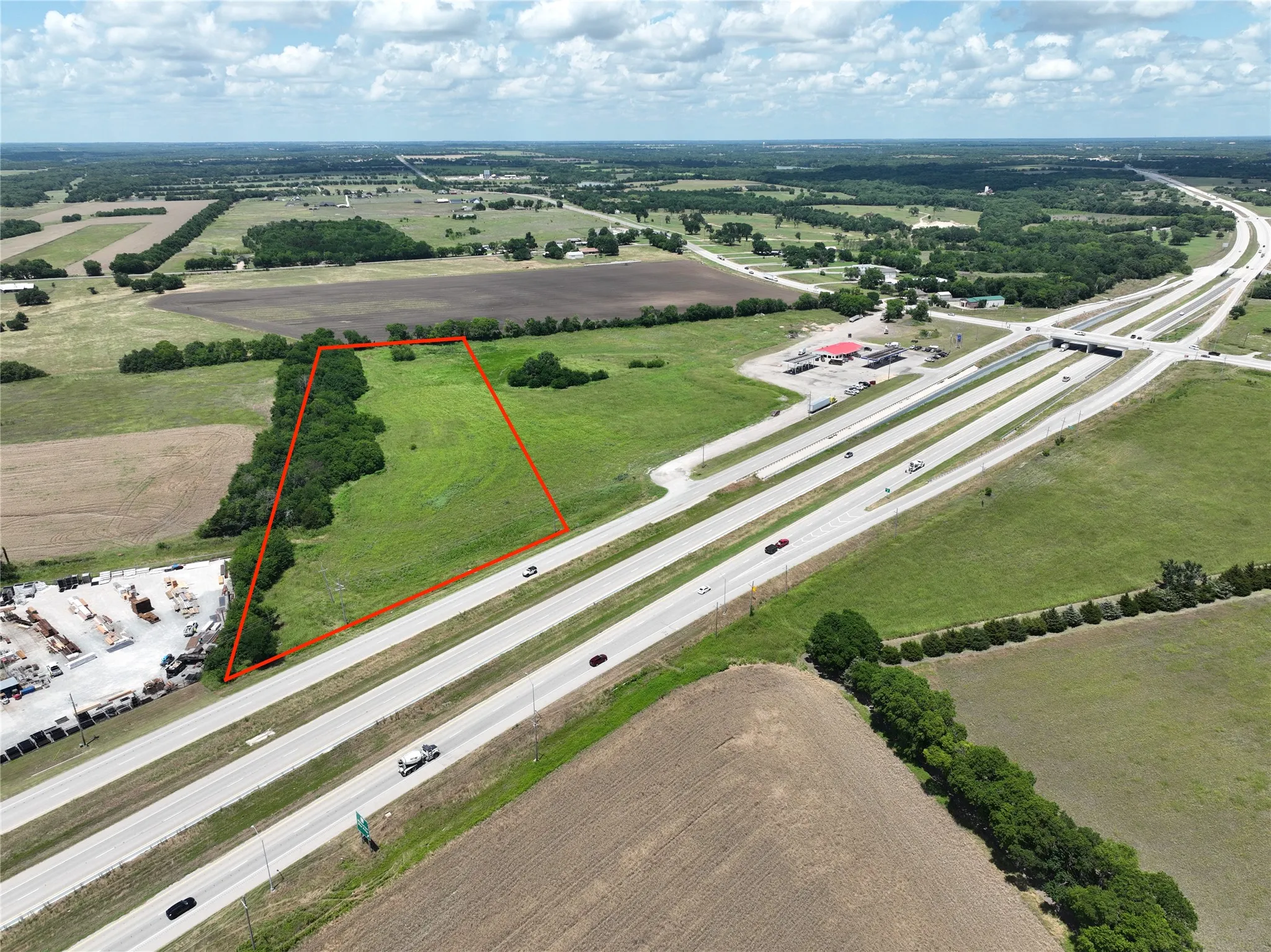 Expansive undeveloped land featuring a natural tree line, perimeter adjacent to a highway, and surrounding agricultural areas
