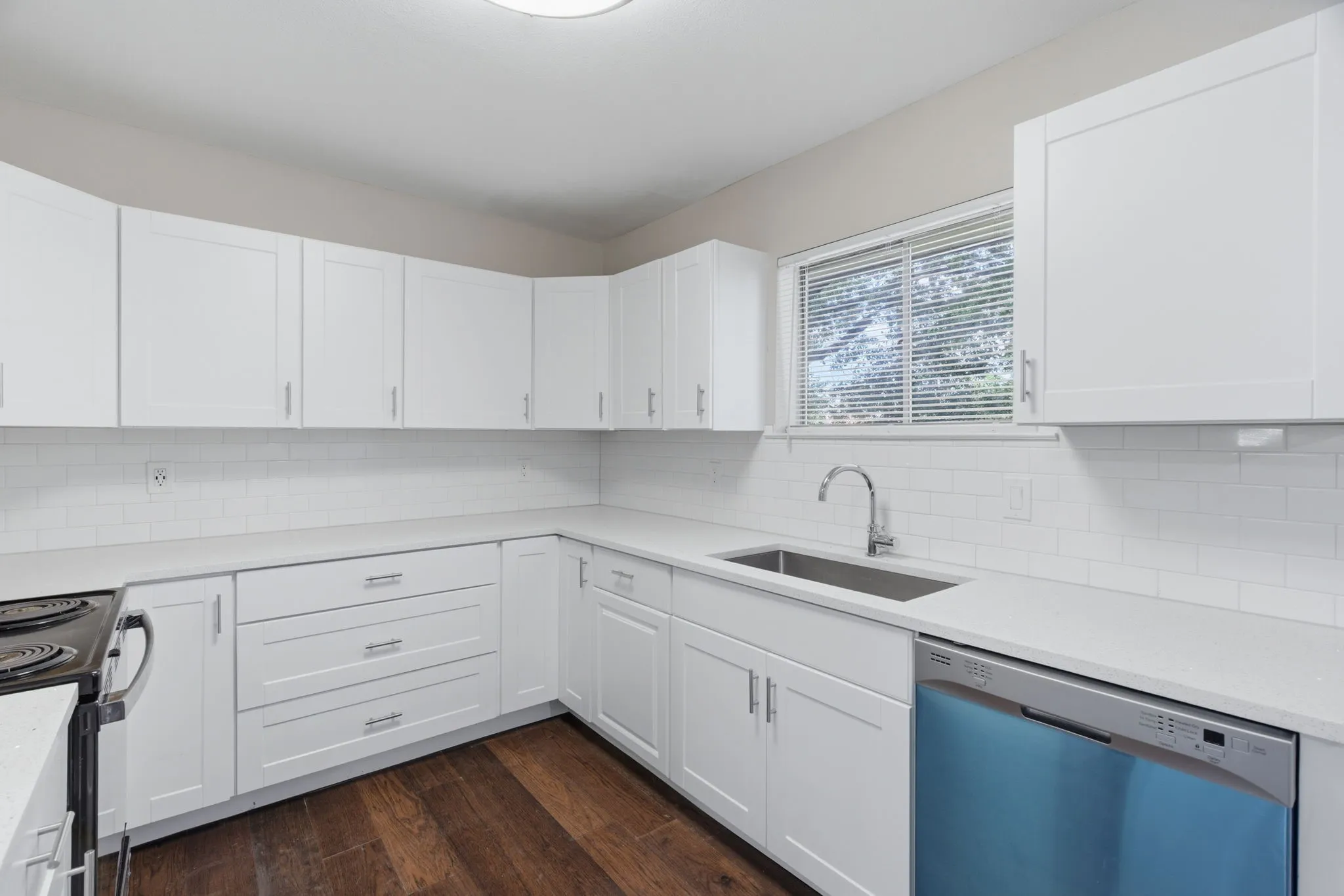 Modern kitchen featuring white shaker cabinetry, light countertops, subway tile backsplash, stainless steel sink with gooseneck faucet, and wood-finish flooring
