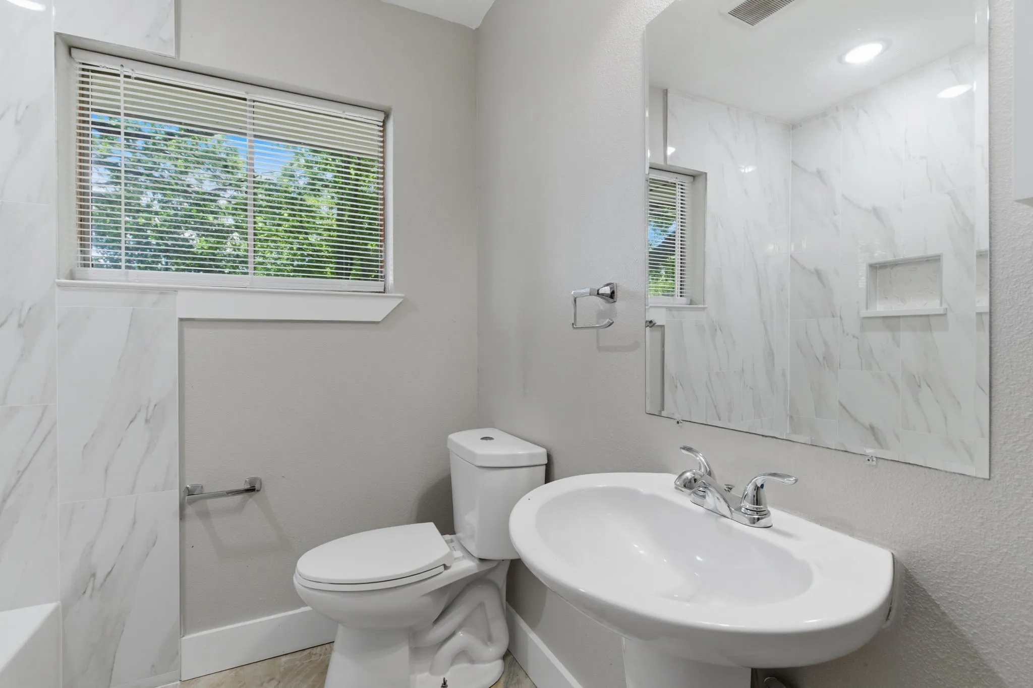 Bathroom featuring a pedestal sink with chrome fixtures, a toilet, and a window with blinds