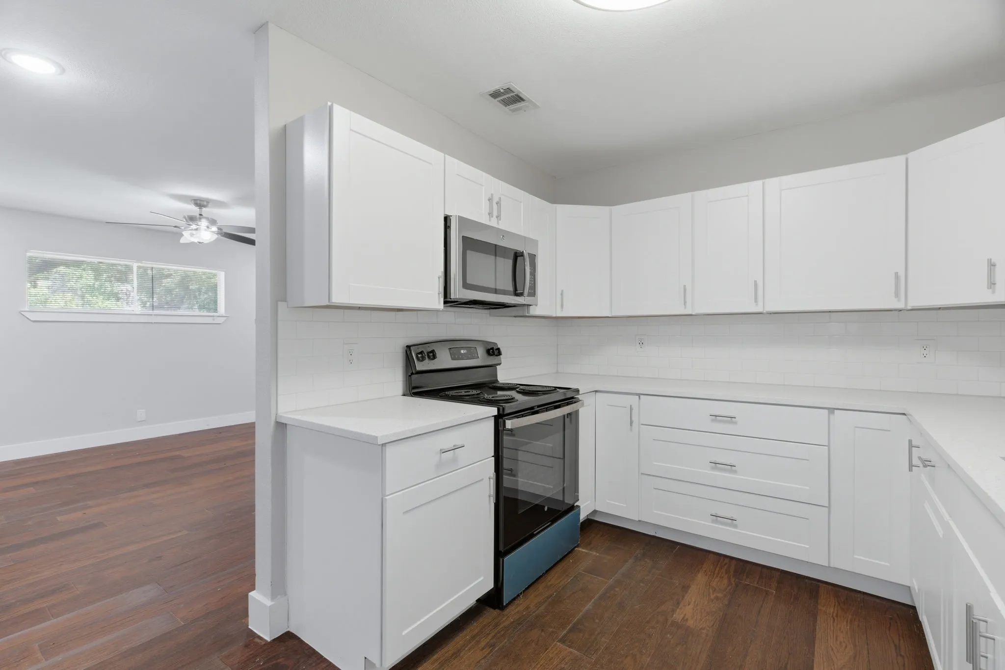 Modern kitchen featuring white shaker cabinetry, stainless steel appliances, white quartz countertops, subway tile backsplash, and dark wood-finish flooring