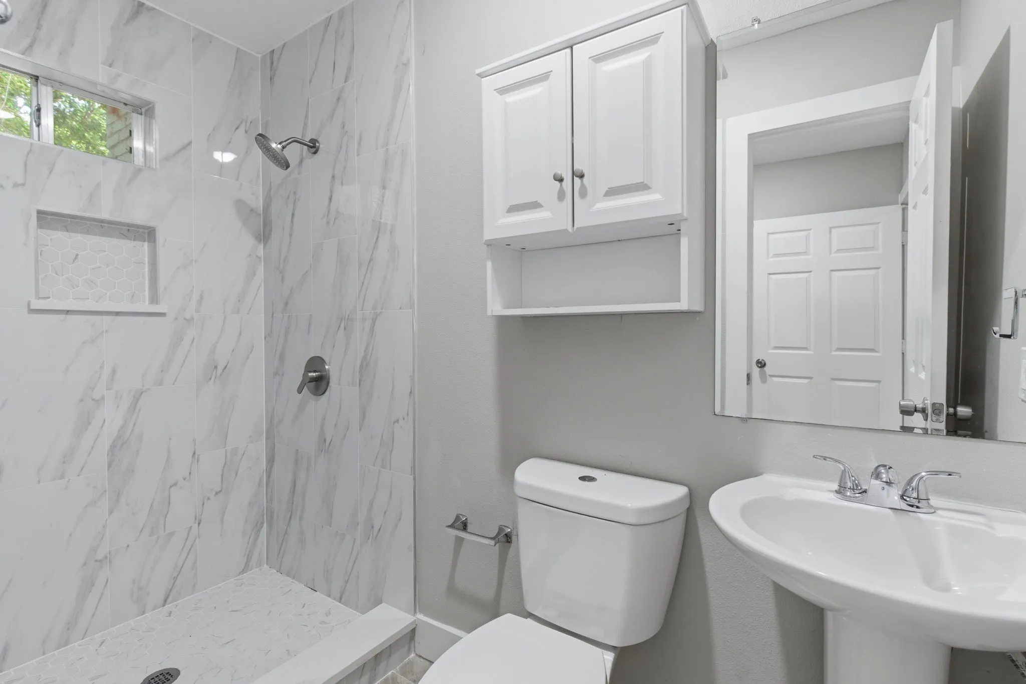 Bathroom featuring a walk-in shower with large format tile, a tiled shower niche, a chrome shower head and faucet, and a horizontally-oriented window