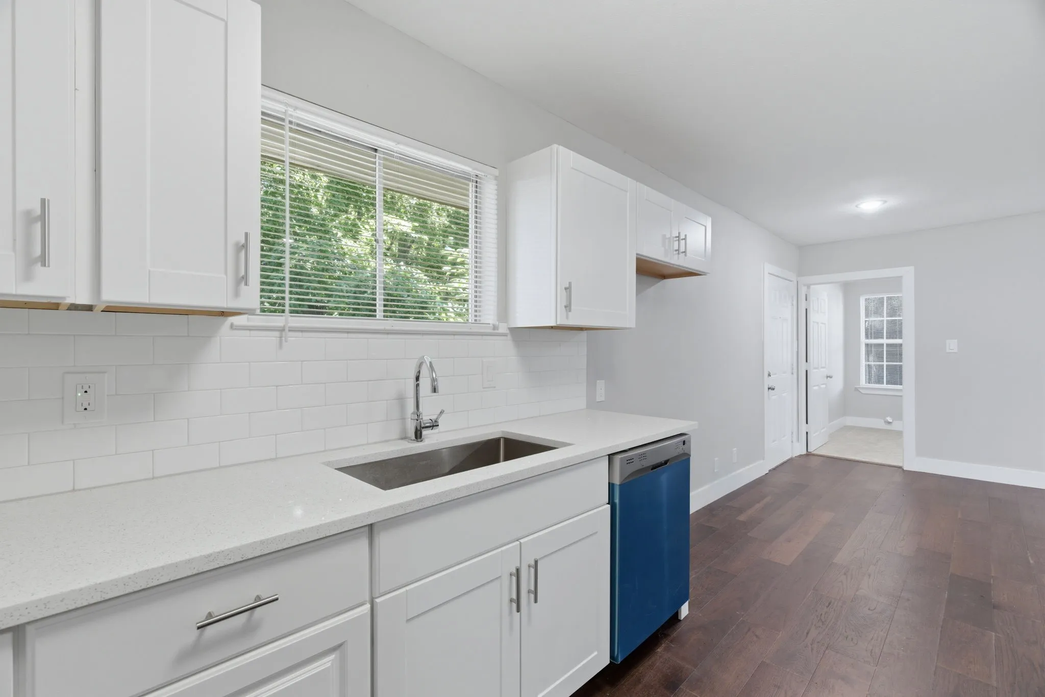 Kitchen area featuring white shaker-style cabinetry, a stainless steel sink, a modern faucet, white subway tile backsplash, and light-toned countertops