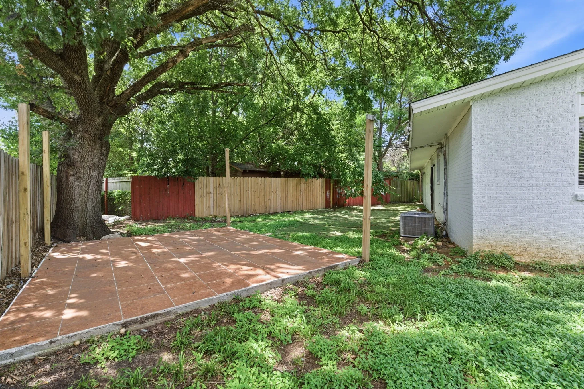 Spacious backyard with mature tree, a tiled patio area, and perimeter fencing