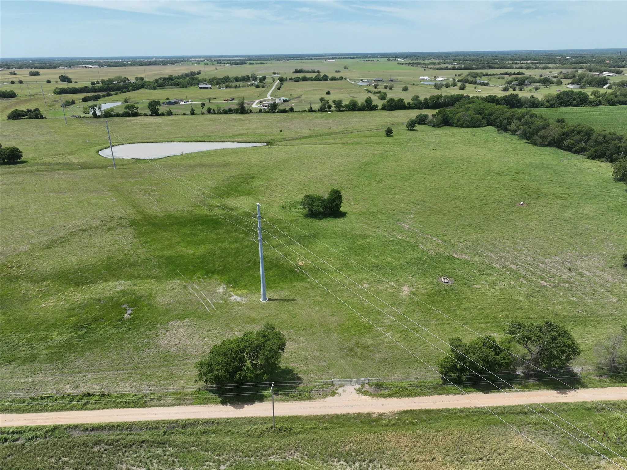 Expansive land parcel featuring a natural pond, a dirt road bordering the property, scattered mature trees, and a power line