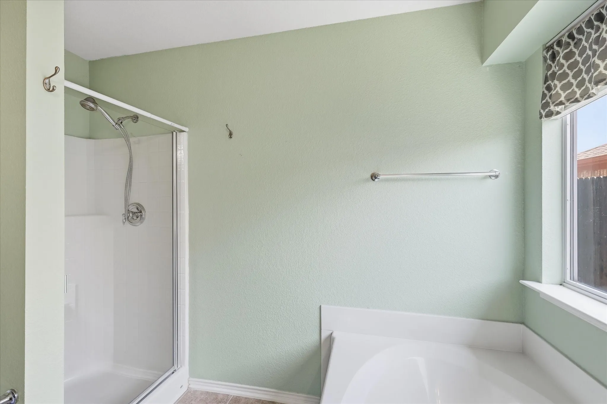 Bathroom featuring a glass-enclosed shower, a built-in tub, and a window with a patterned valance