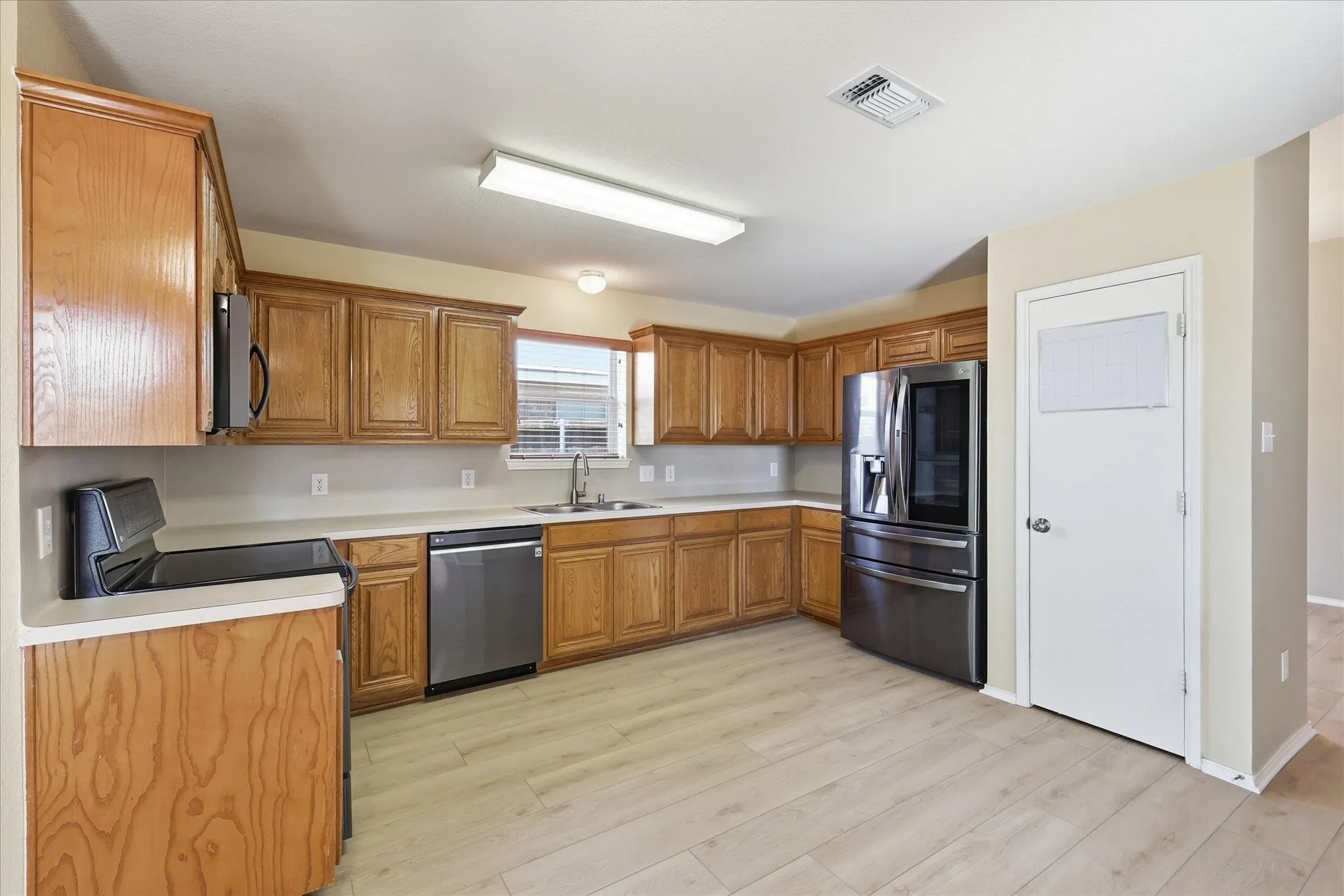 Kitchen with wood-finish cabinetry, light countertops, and stainless steel appliances including a refrigerator, dishwasher, and range