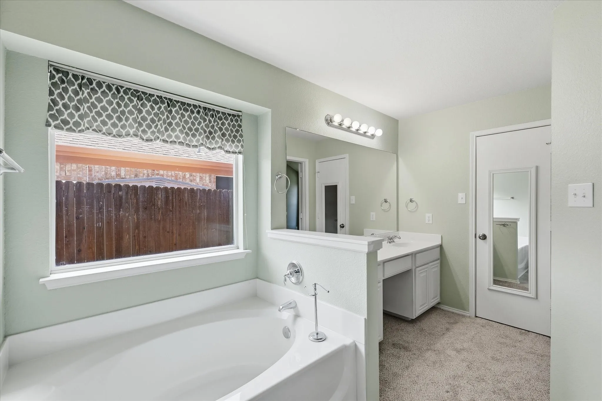 Built-in soaking tub with chrome fixtures and a window featuring a patterned valance