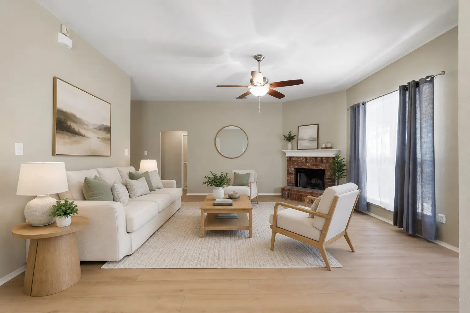 Living area with light wood-finish flooring, a brick fireplace with a white mantel, and a ceiling fan. Virtually Staged.
