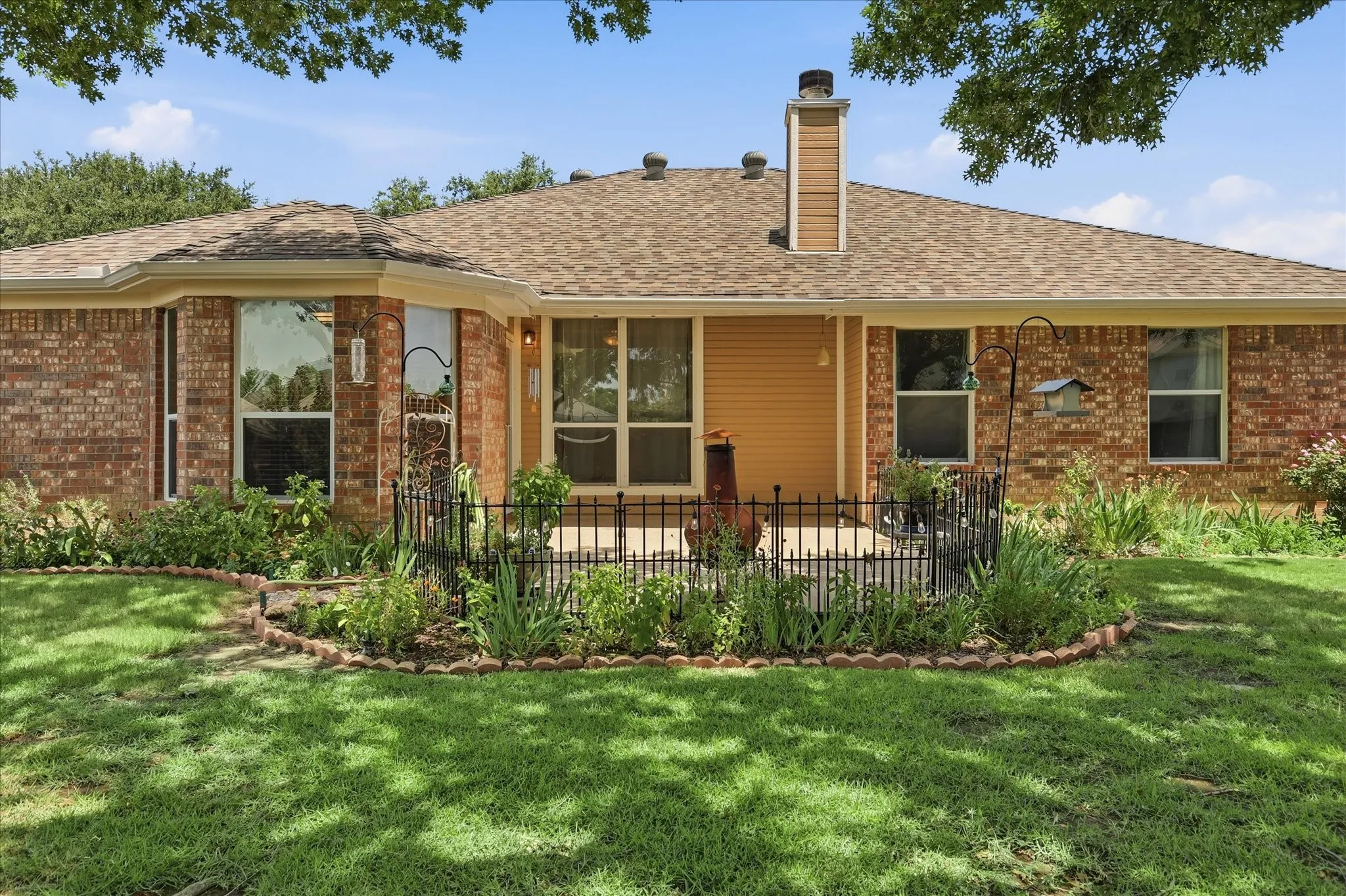 Brick exterior featuring a private patio, mature landscaping, bay window, and a shingled roof