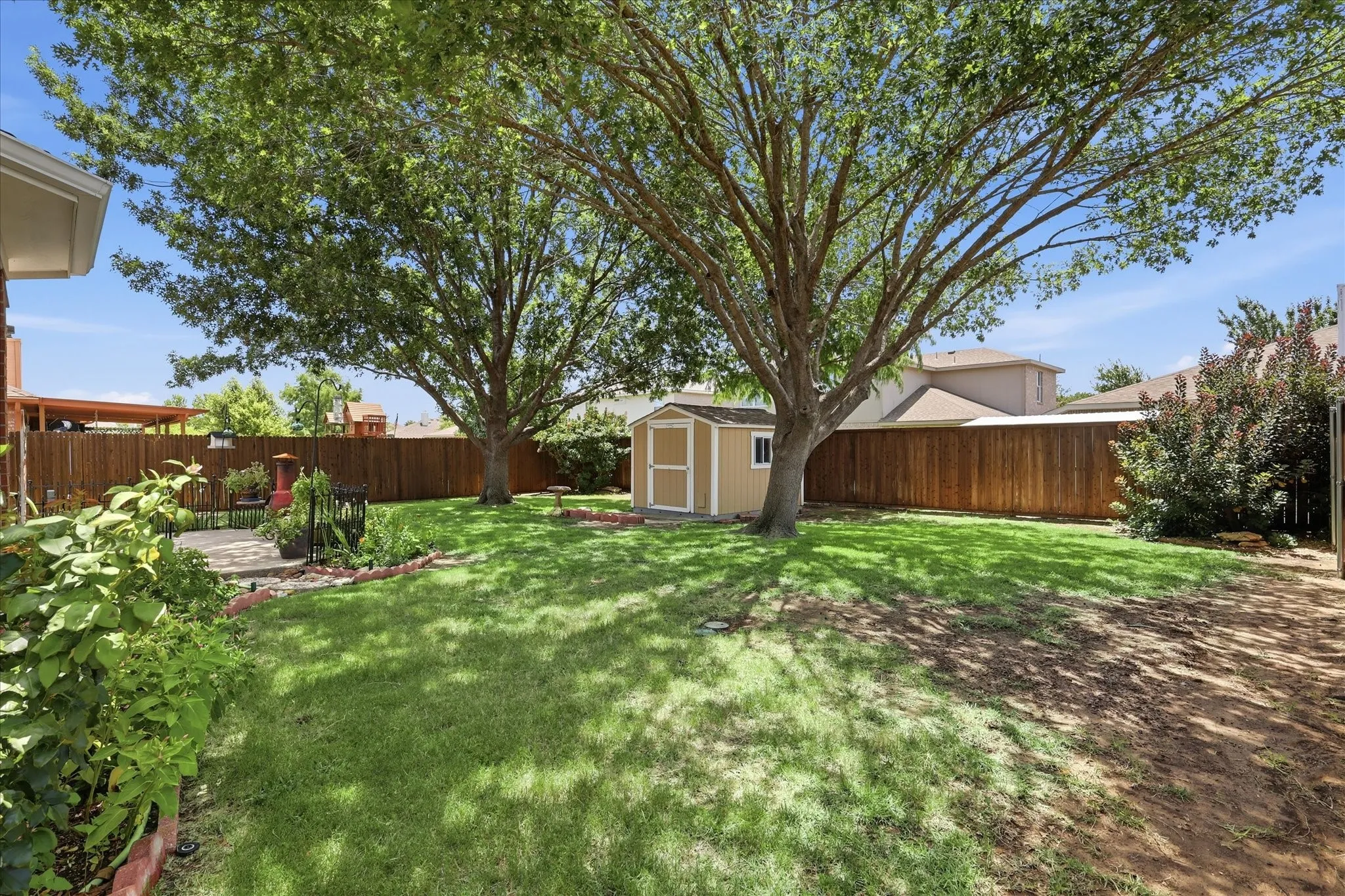 Expansive backyard featuring a manicured lawn, established shade trees, a storage shed, a privacy fence, and a stone patio area