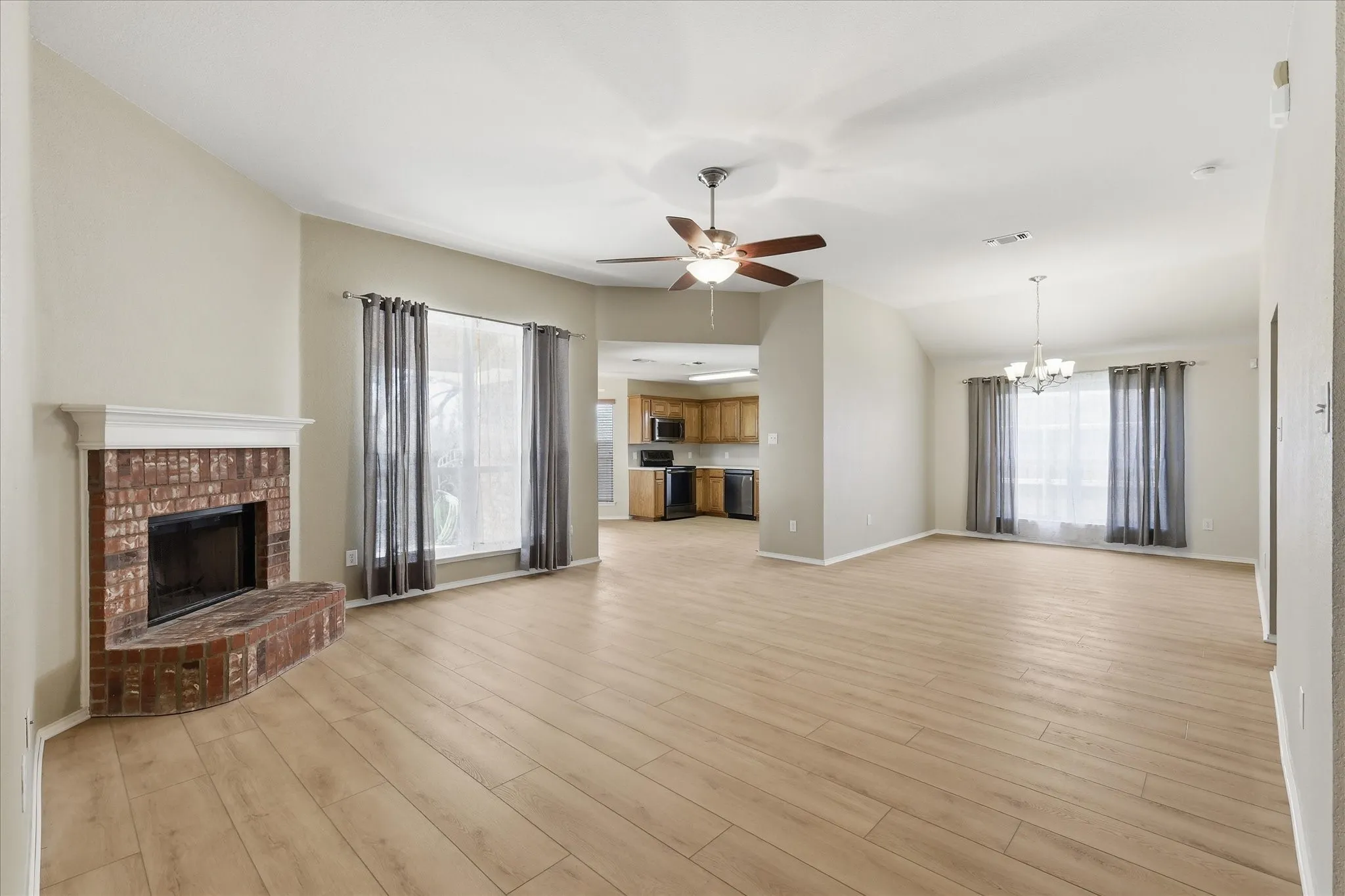 Spacious living area featuring wood-finish flooring, a brick fireplace with a white mantel, and vaulted ceilings