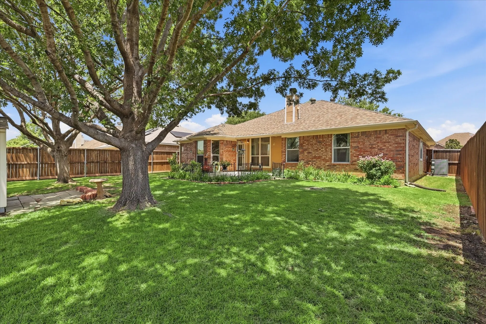 Expansive backyard featuring a manicured lawn, mature shade trees, and a privacy fence