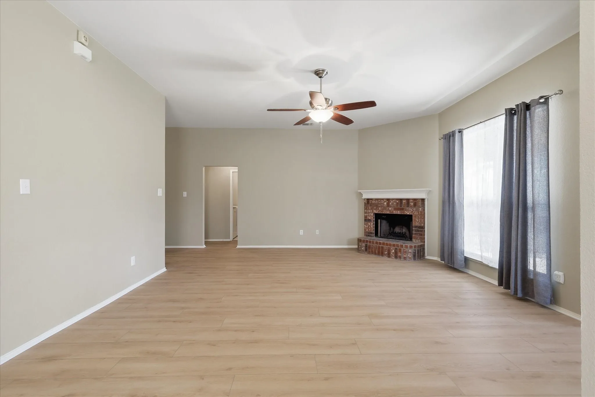 Spacious living area featuring wood-finish flooring, a brick fireplace with a white mantel, and a ceiling fan