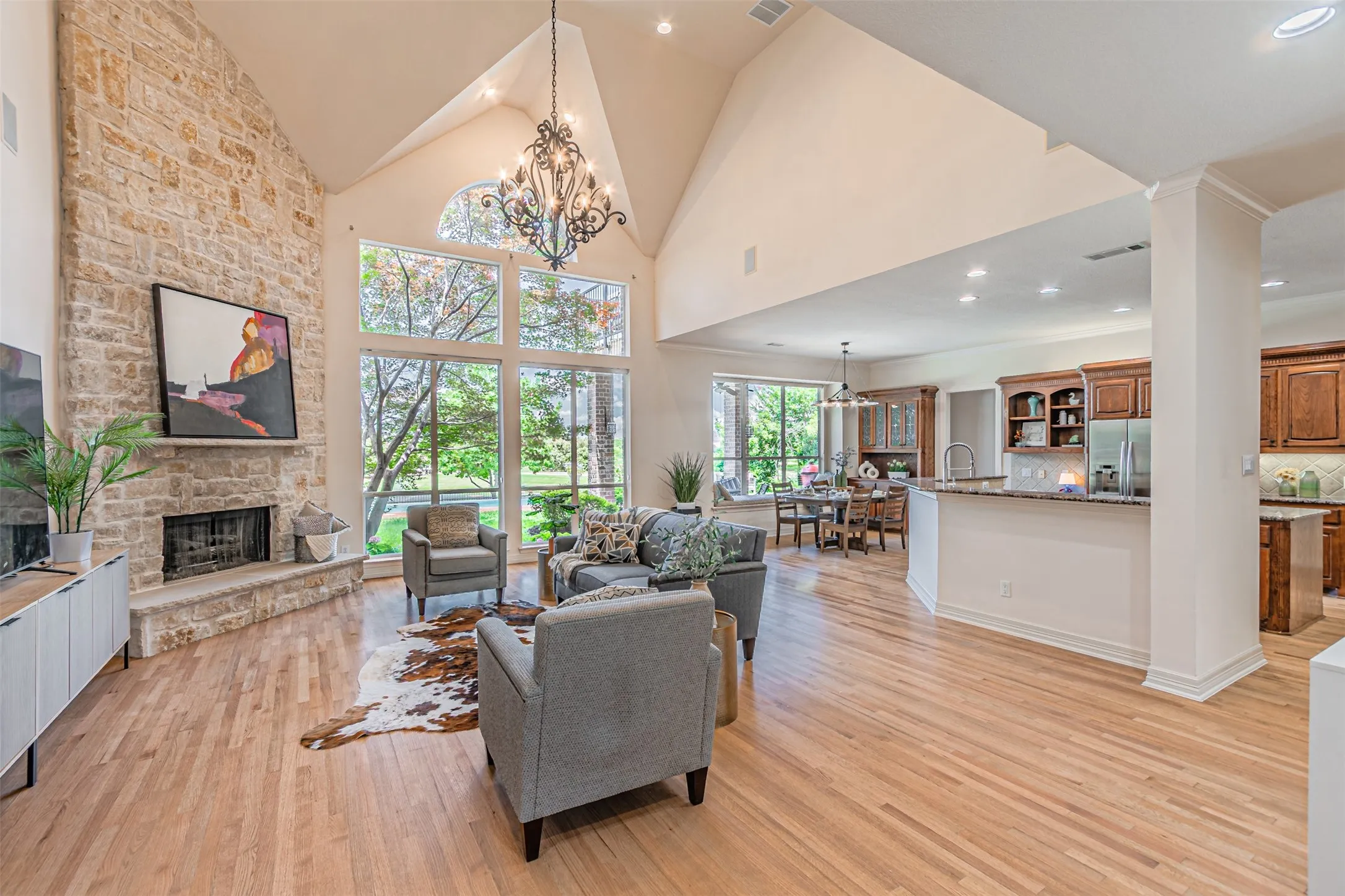 Living space featuring a stone fireplace, vaulted ceiling with chandelier, and a wall of windows