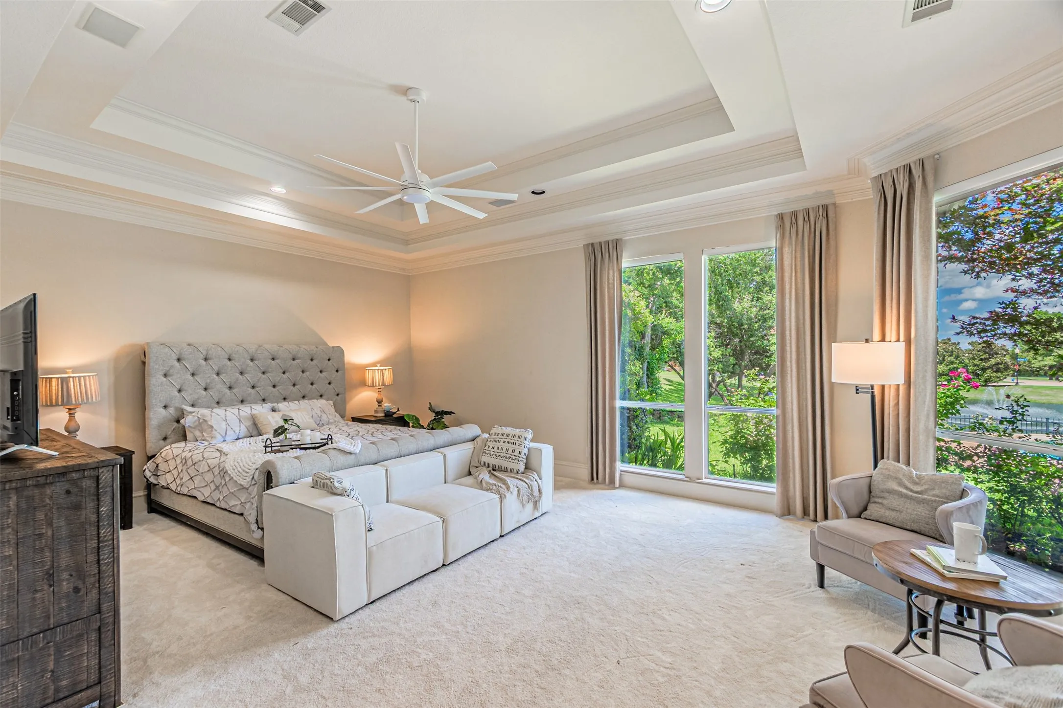 Spacious bedroom featuring multiple large windows, tray ceiling with crown molding, and recessed lighting