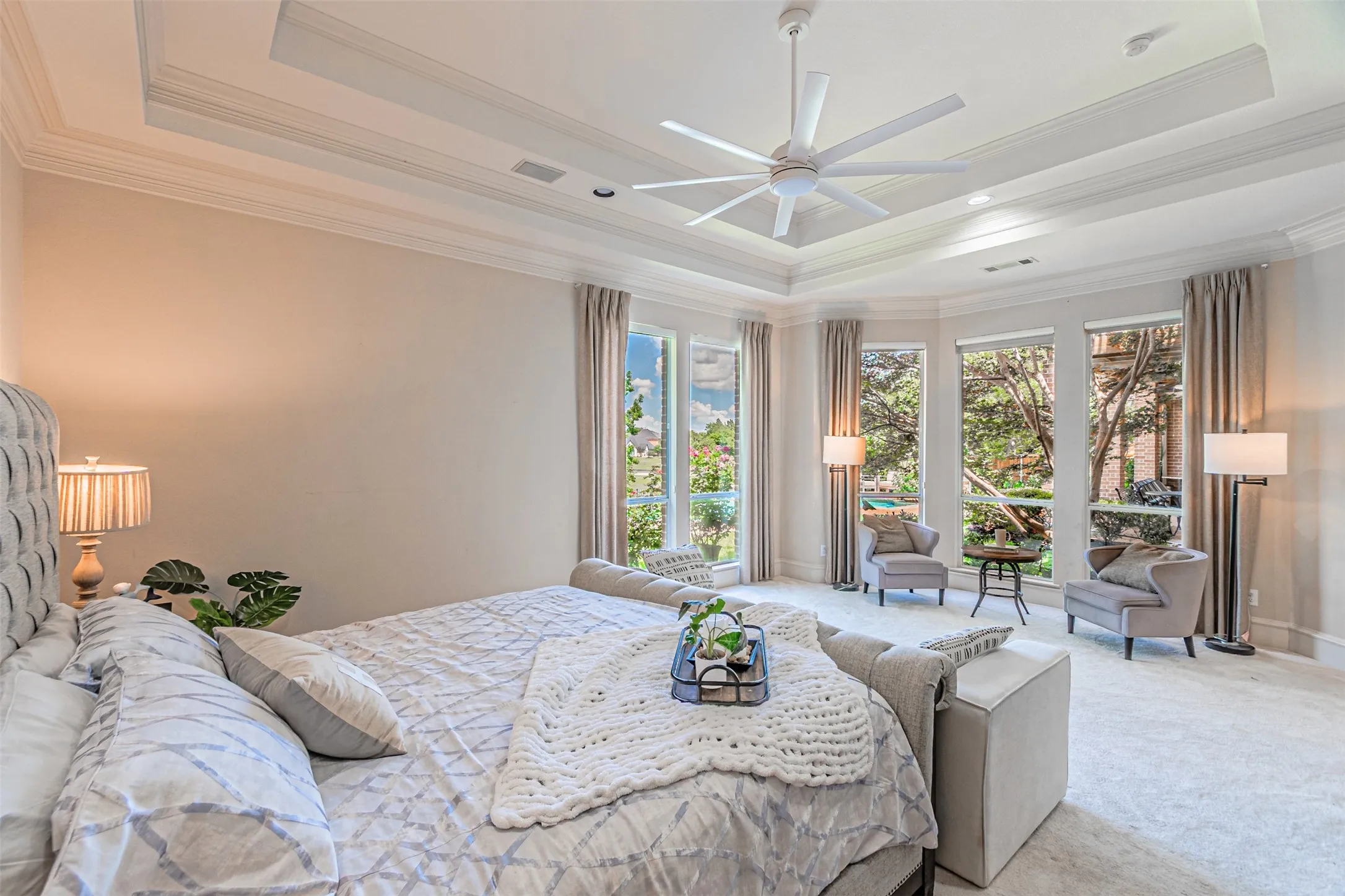 Spacious room featuring multiple bay windows with neutral drapes, a multi-tiered tray ceiling with crown molding, a ceiling fan, and light-toned carpeting