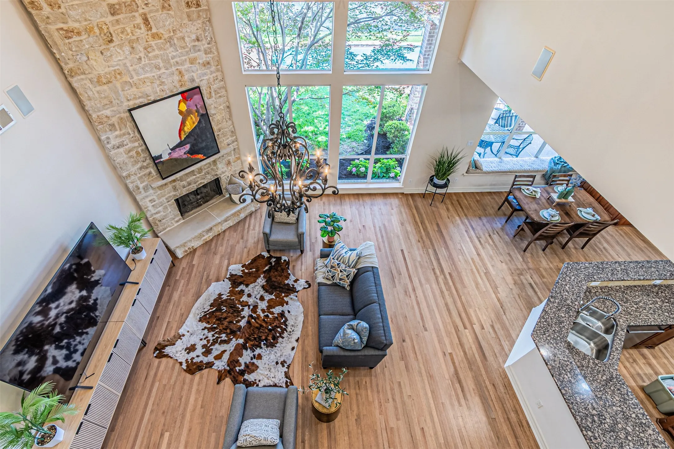 Two-story living area featuring a stone fireplace, large windows, a decorative chandelier, and wood-finish flooring