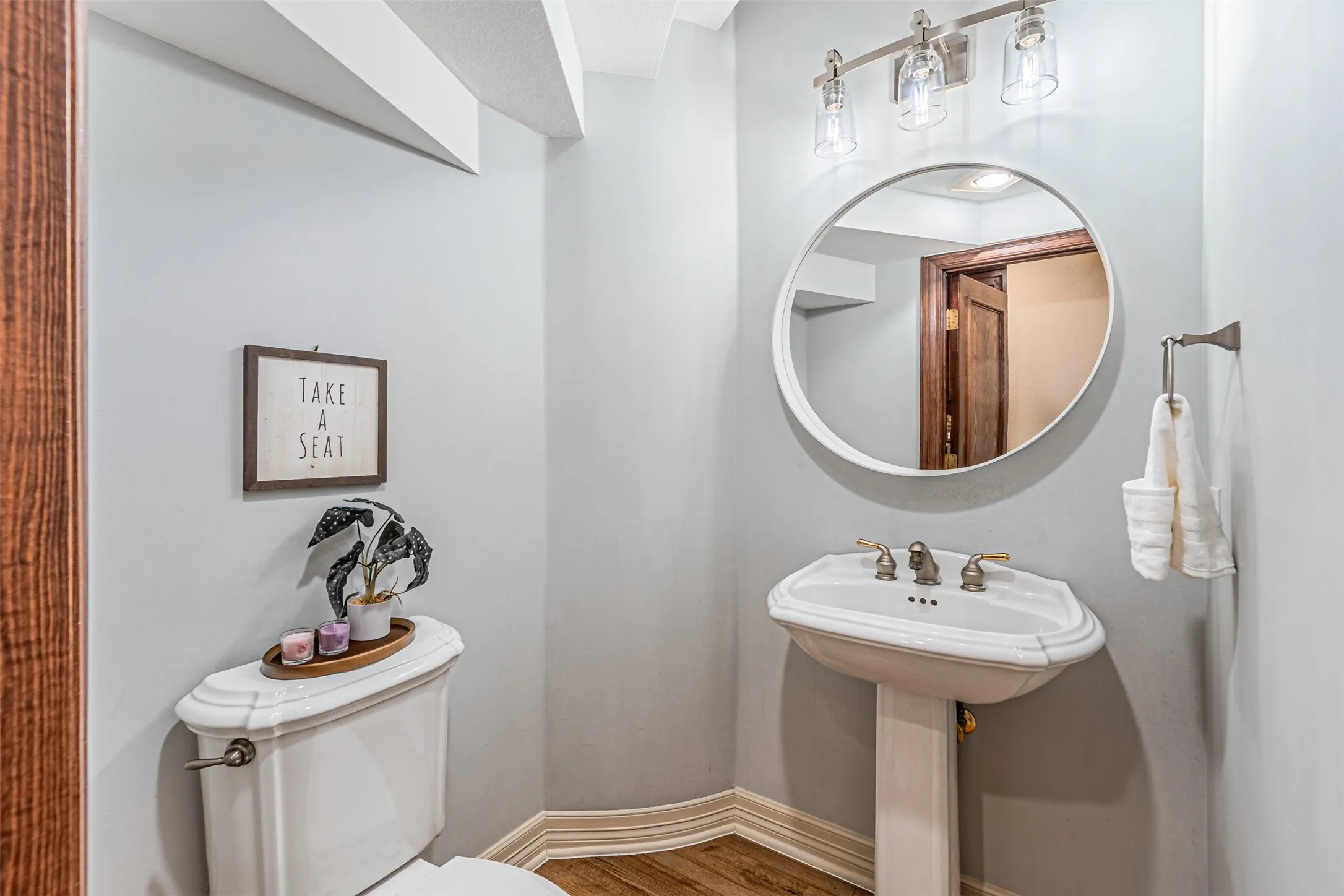 Pedestal sink with brass-finish faucet, circular mirror, and triple vanity light fixture