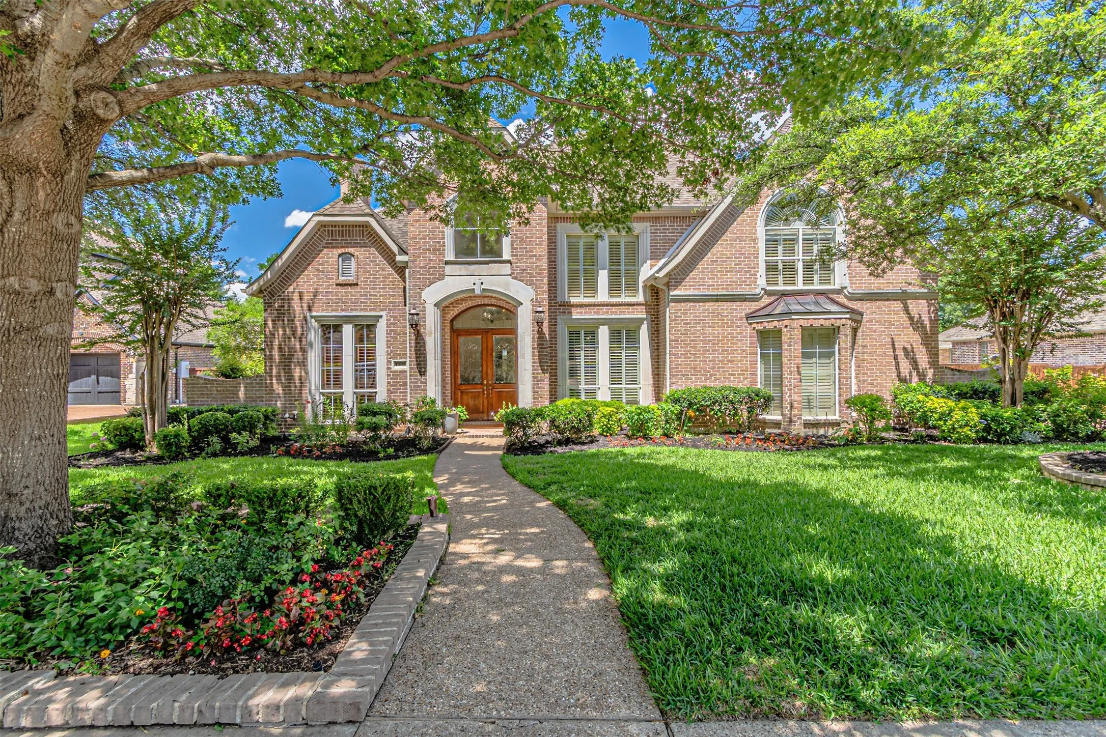 Traditional brick exterior featuring a prominent arched entry with double wood doors, a curved walkway, and established landscaping