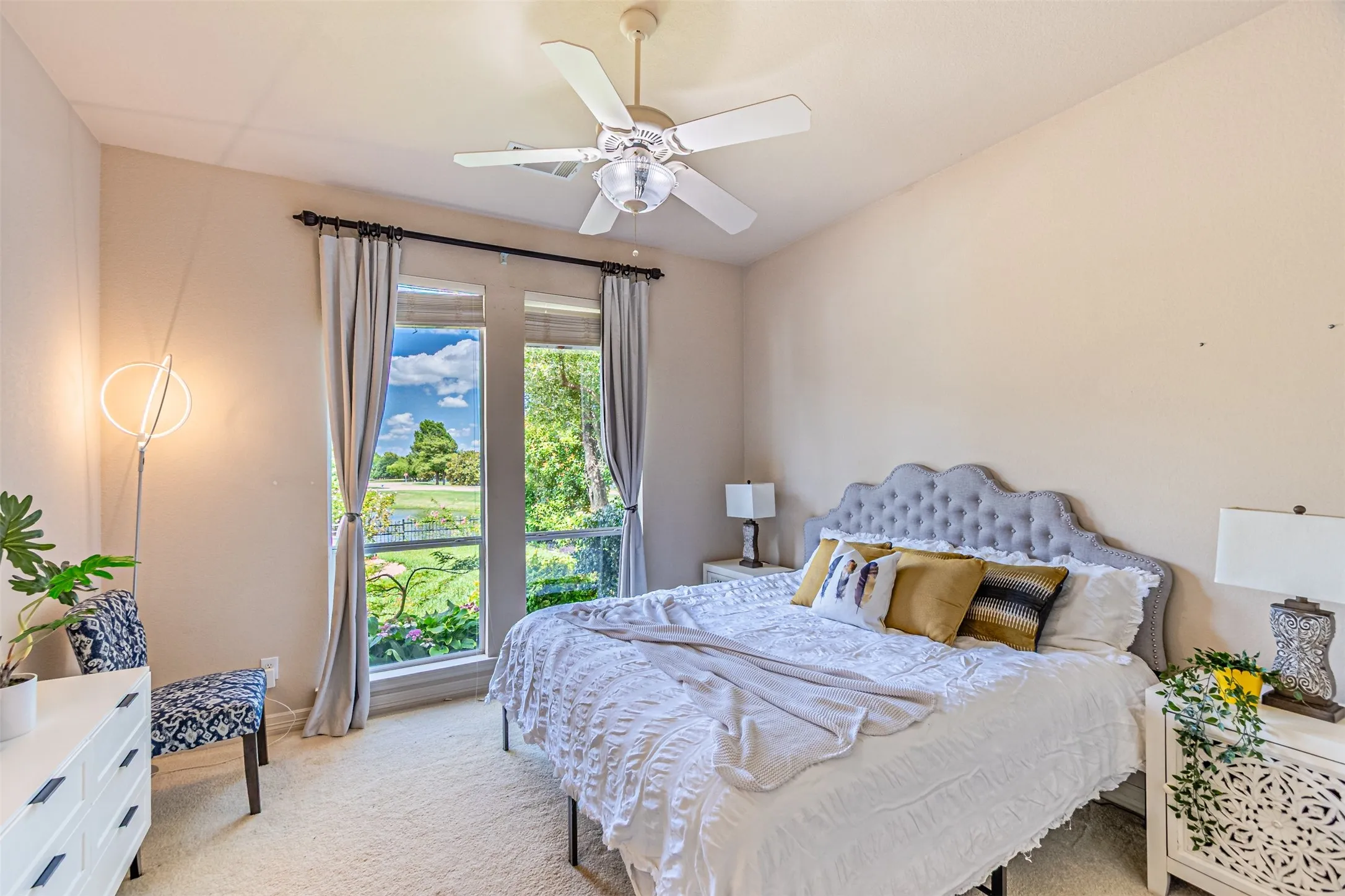 Bedroom featuring expansive windows with serene outdoor landscaping, neutral wall tones, textured carpeting, and a ceiling fan with integrated lighting