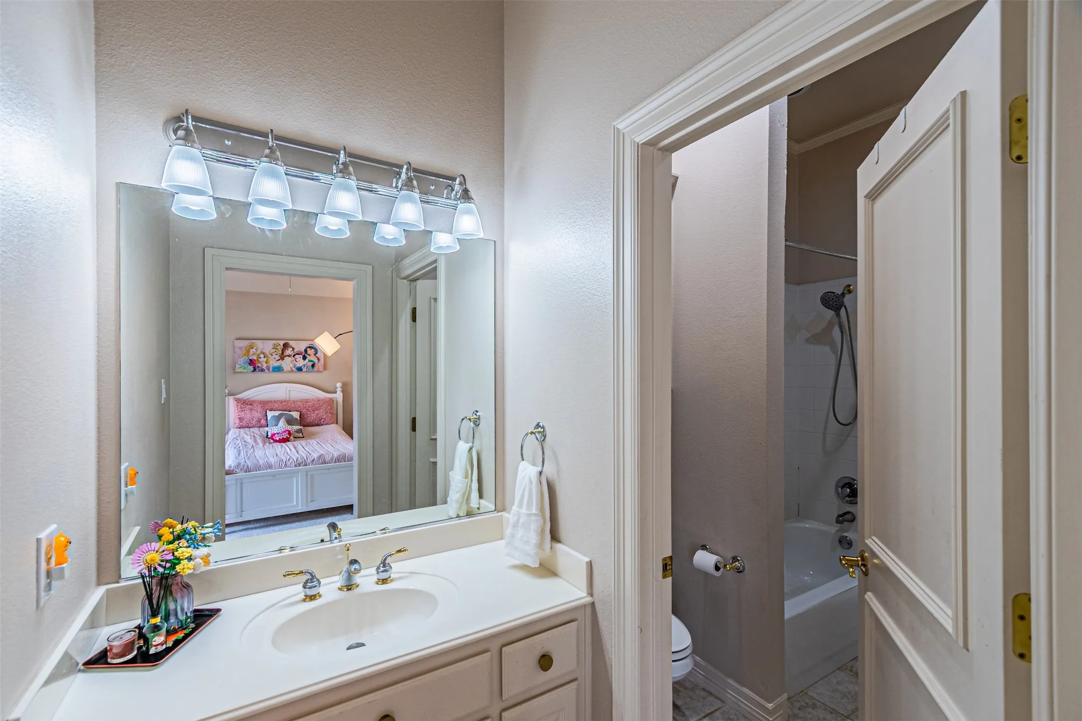 Vanity with an integrated sink, polished brass and chrome-finish faucet, and a wall-mounted mirror with an overhead light fixture
