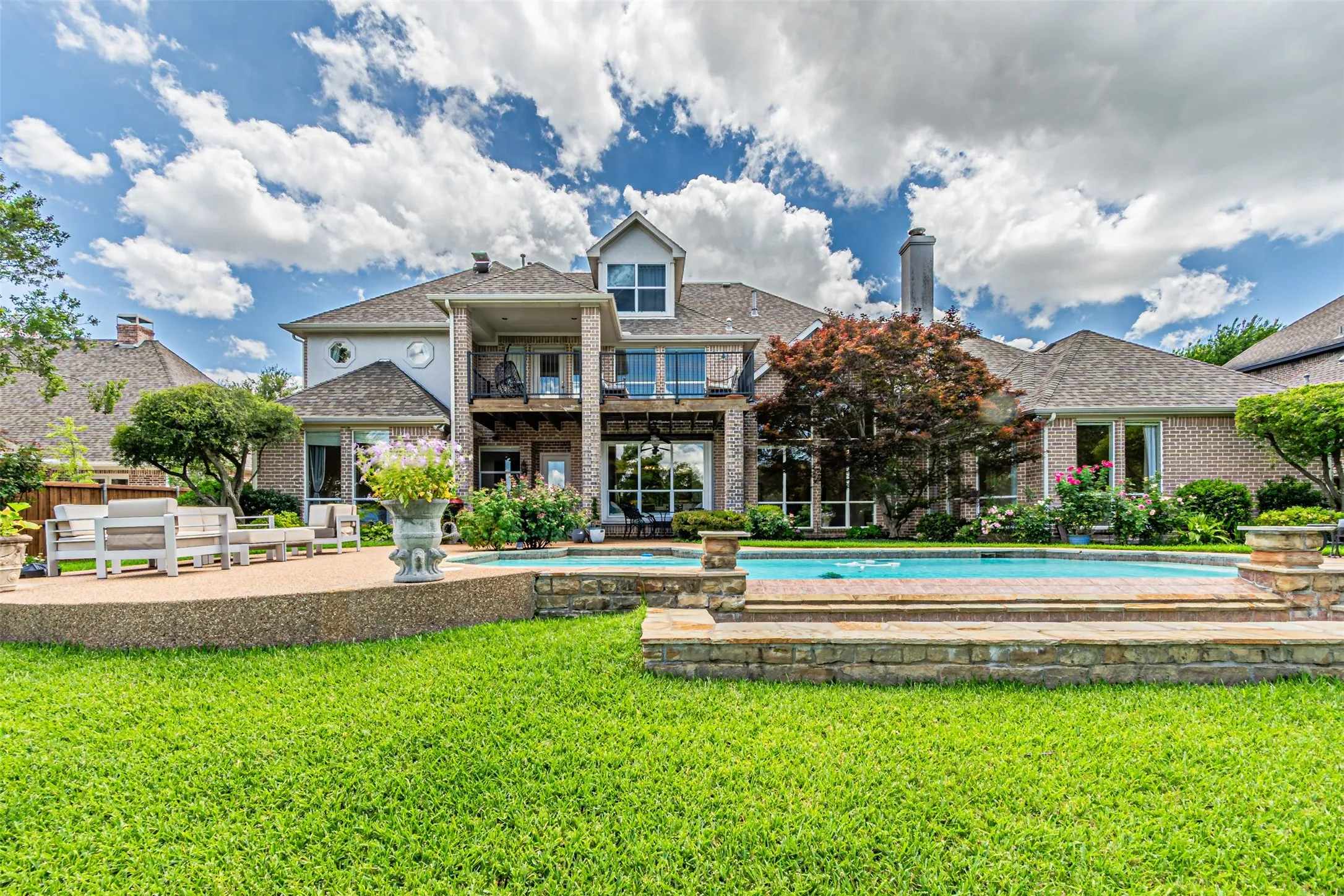 Expansive backyard featuring a rectangular swimming pool with stone surround, a large concrete patio, and a well-maintained lawn