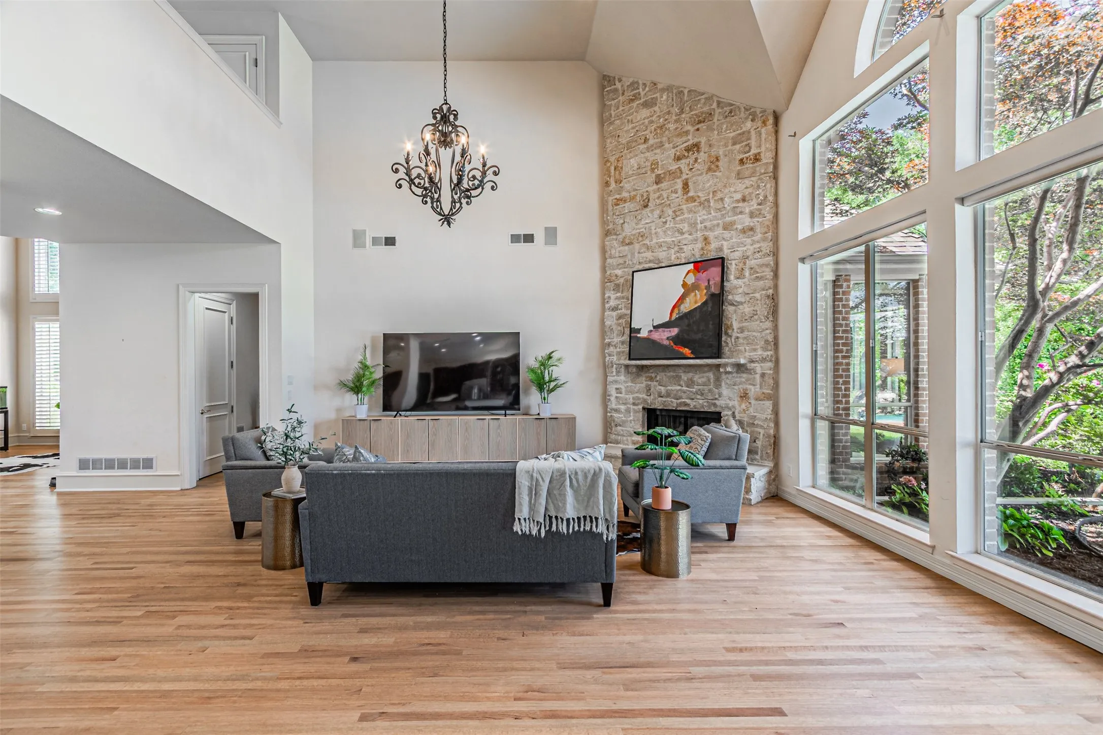 Vaulted living space with expansive window wall, stone fireplace, and wood-finish flooring