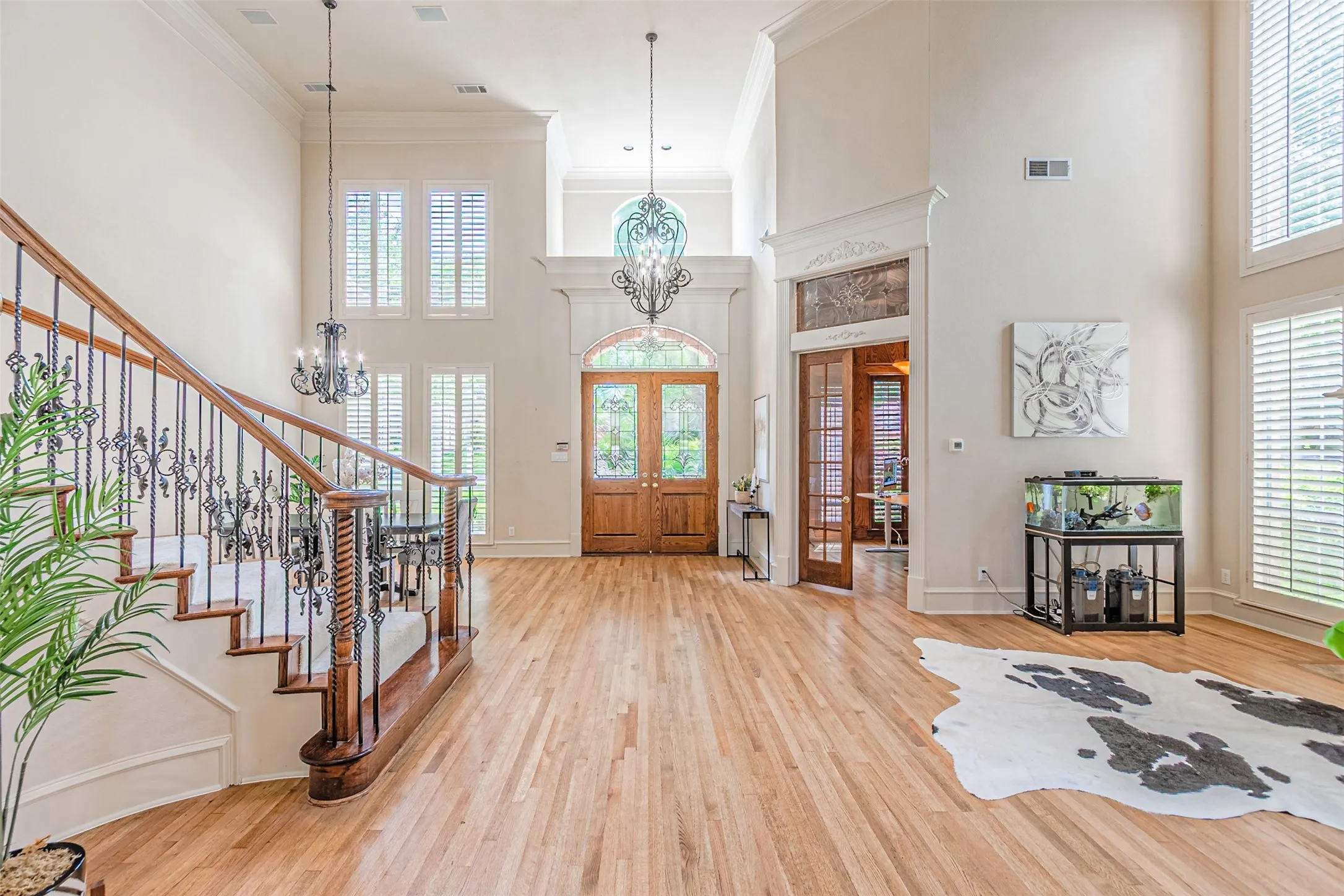 Two-story foyer featuring hardwood flooring, a grand staircase with decorative wrought iron spindles, a double-door entry with arched transom, and multiple tall windows with plantation shutters