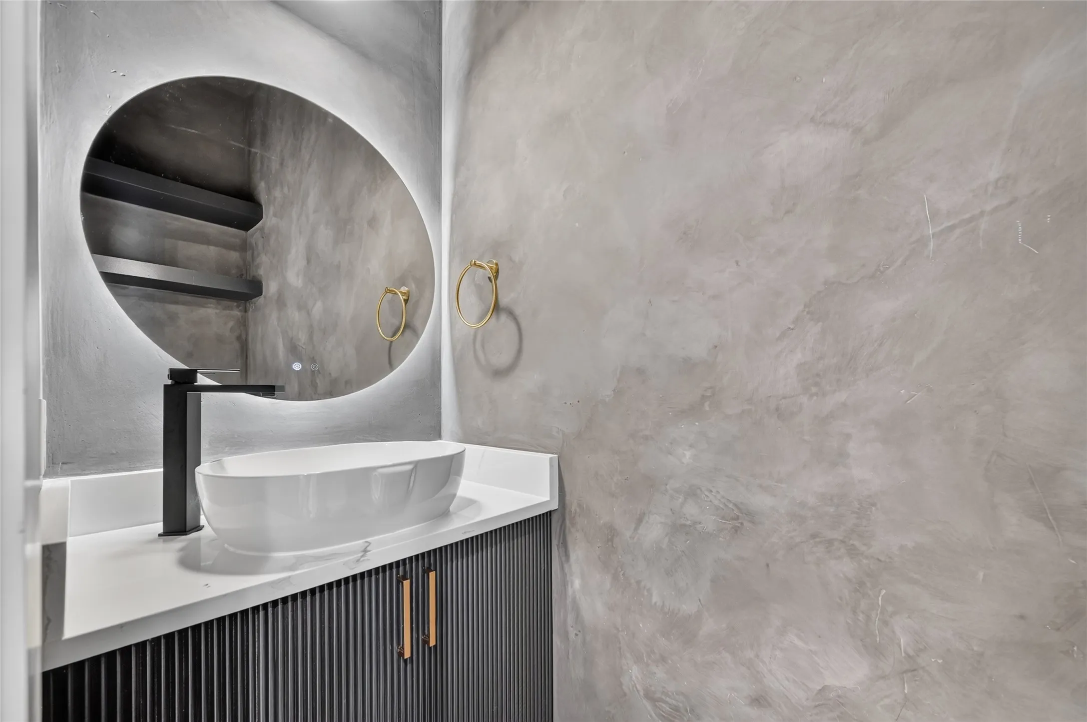 Modern vanity featuring a white vessel sink, matte black faucet, and a lighted oval mirror