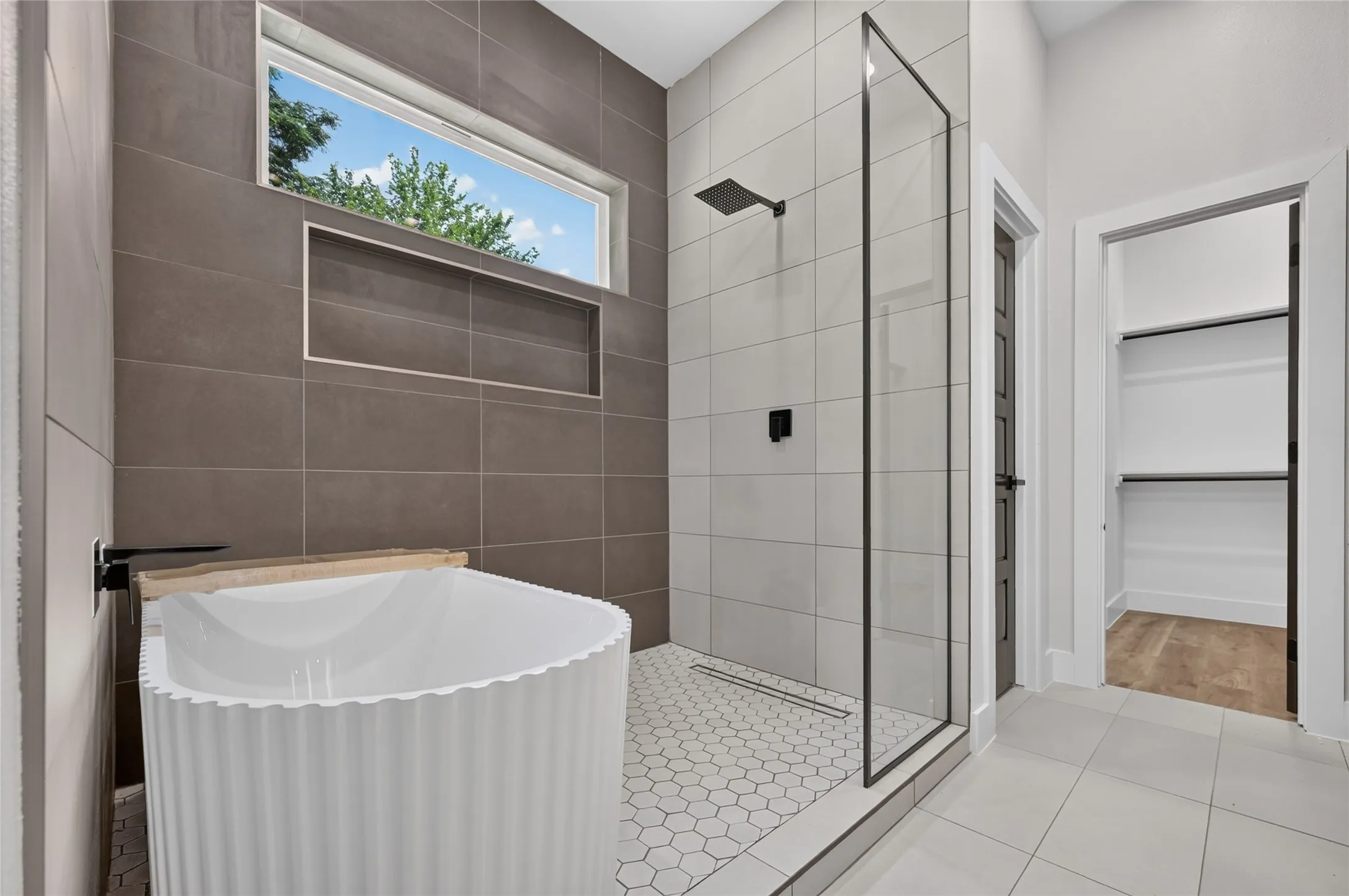Contemporary bathroom featuring a freestanding soaking tub with a matte black wall-mounted faucet, a walk-in shower with a frameless glass enclosure and matte black fixtures, a recessed shower niche, and hexagonal tile flooring