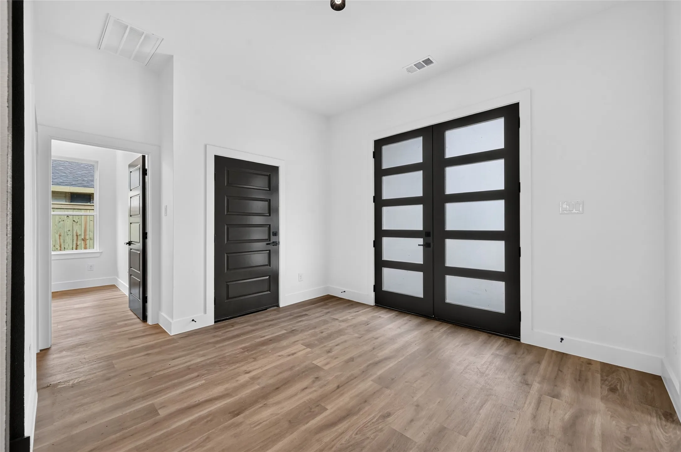 Spacious room featuring wood-finish flooring, white walls, and a pair of modern French doors with frosted glass panels