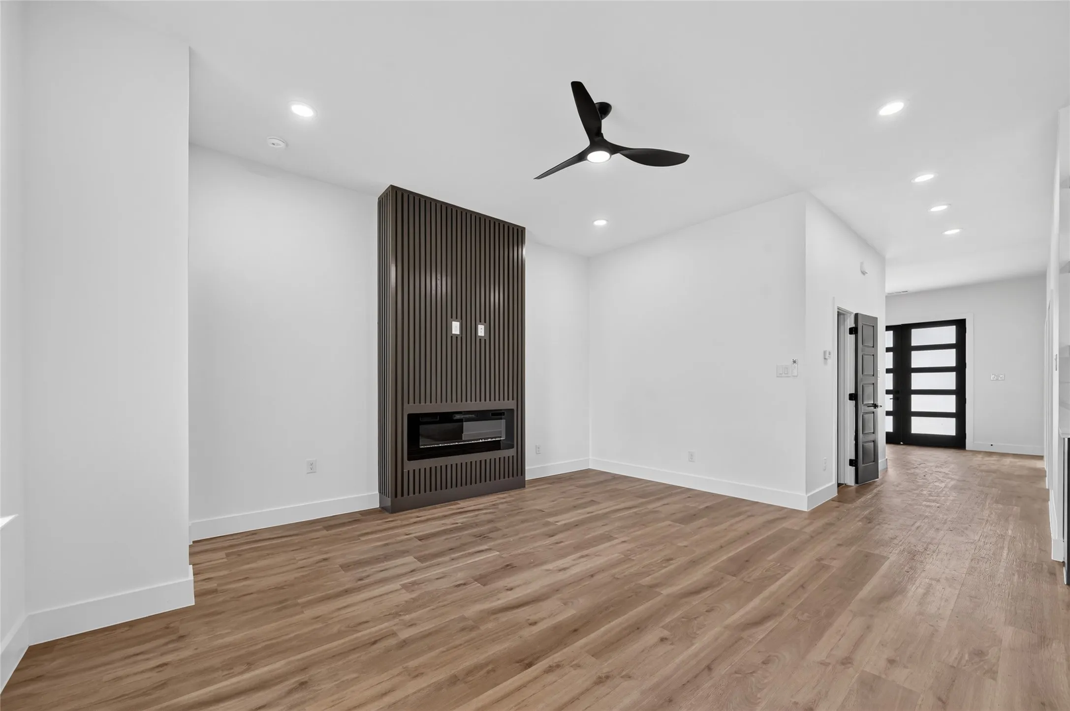 Spacious room featuring wood-finish flooring, a built-in fireplace with a fluted panel surround, recessed lighting, and a modern ceiling fan