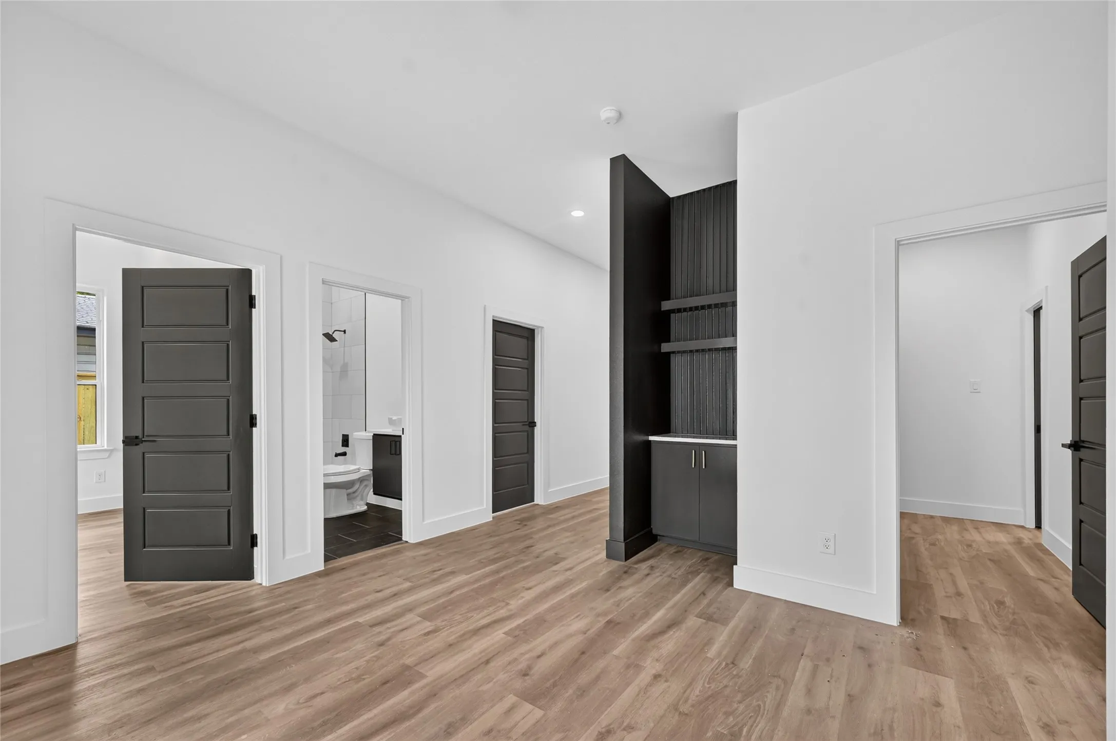 Wood-finish flooring throughout, complemented by white walls and modern dark panel doors