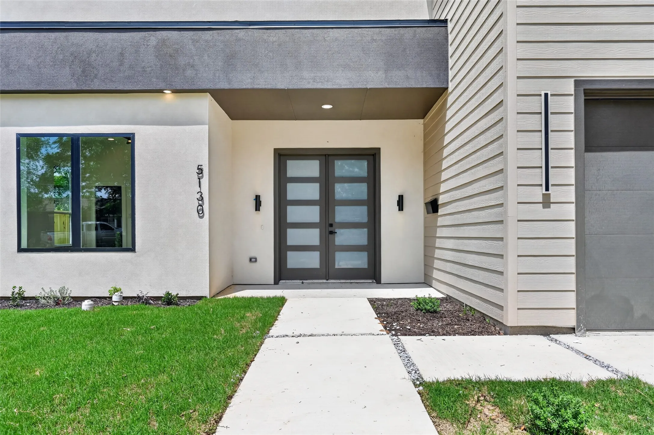 Contemporary architectural facade featuring a double entry door with frosted glass panels, smooth stucco finishes, and horizontal siding