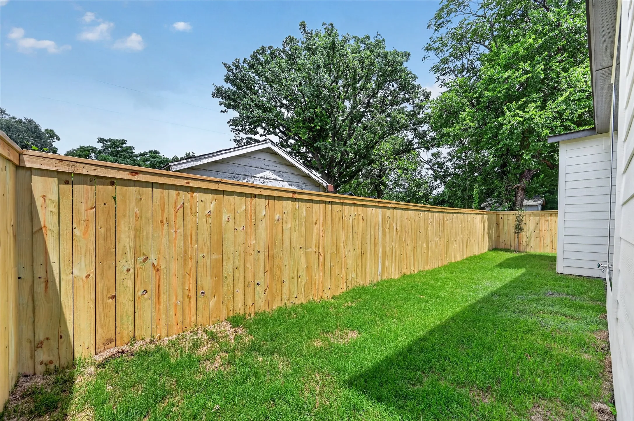 Private backyard featuring a new wood privacy fence, expansive green lawn, and exterior siding