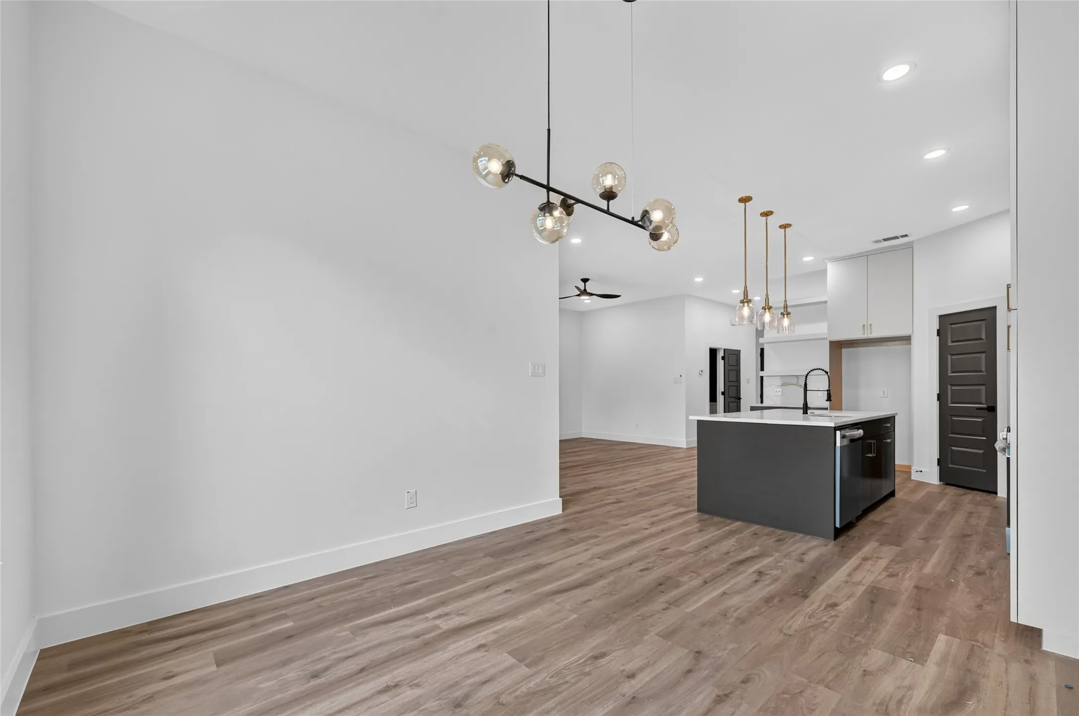 Open-concept interior featuring wood-finish flooring, a modern chandelier, recessed lighting, a kitchen island with sink and integrated dishwasher, and contrasting dark interior doors