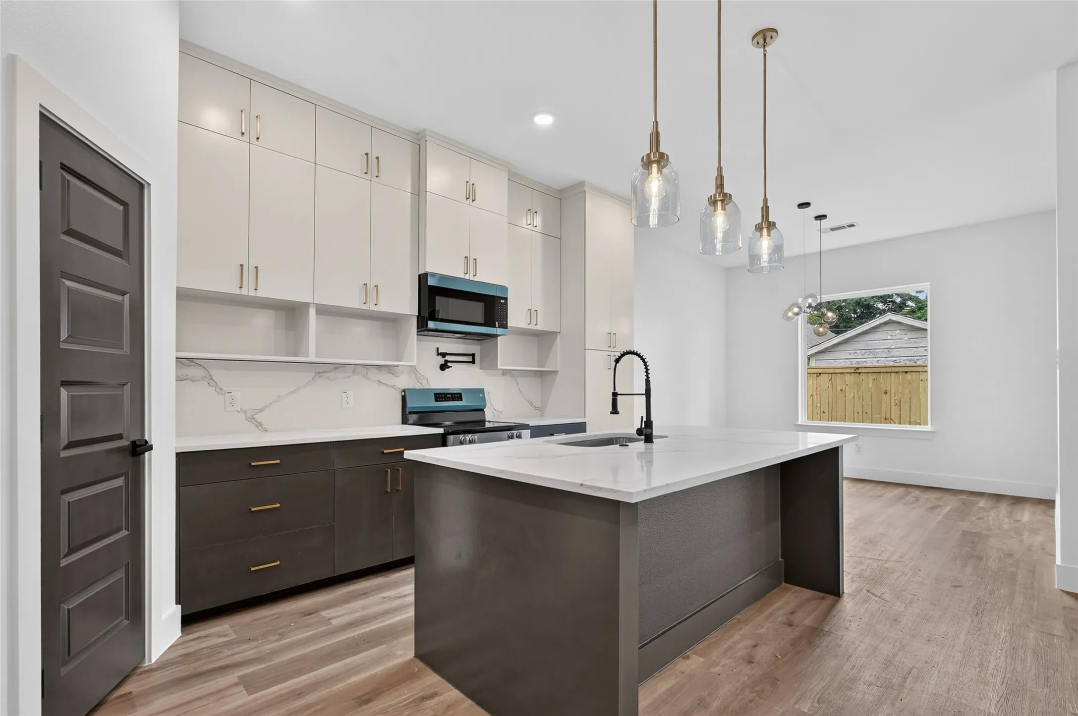 Modern kitchen featuring two-tone cabinetry with gold-tone hardware, a waterfall island with a gooseneck faucet, a patterned backsplash, and wood-finish flooring