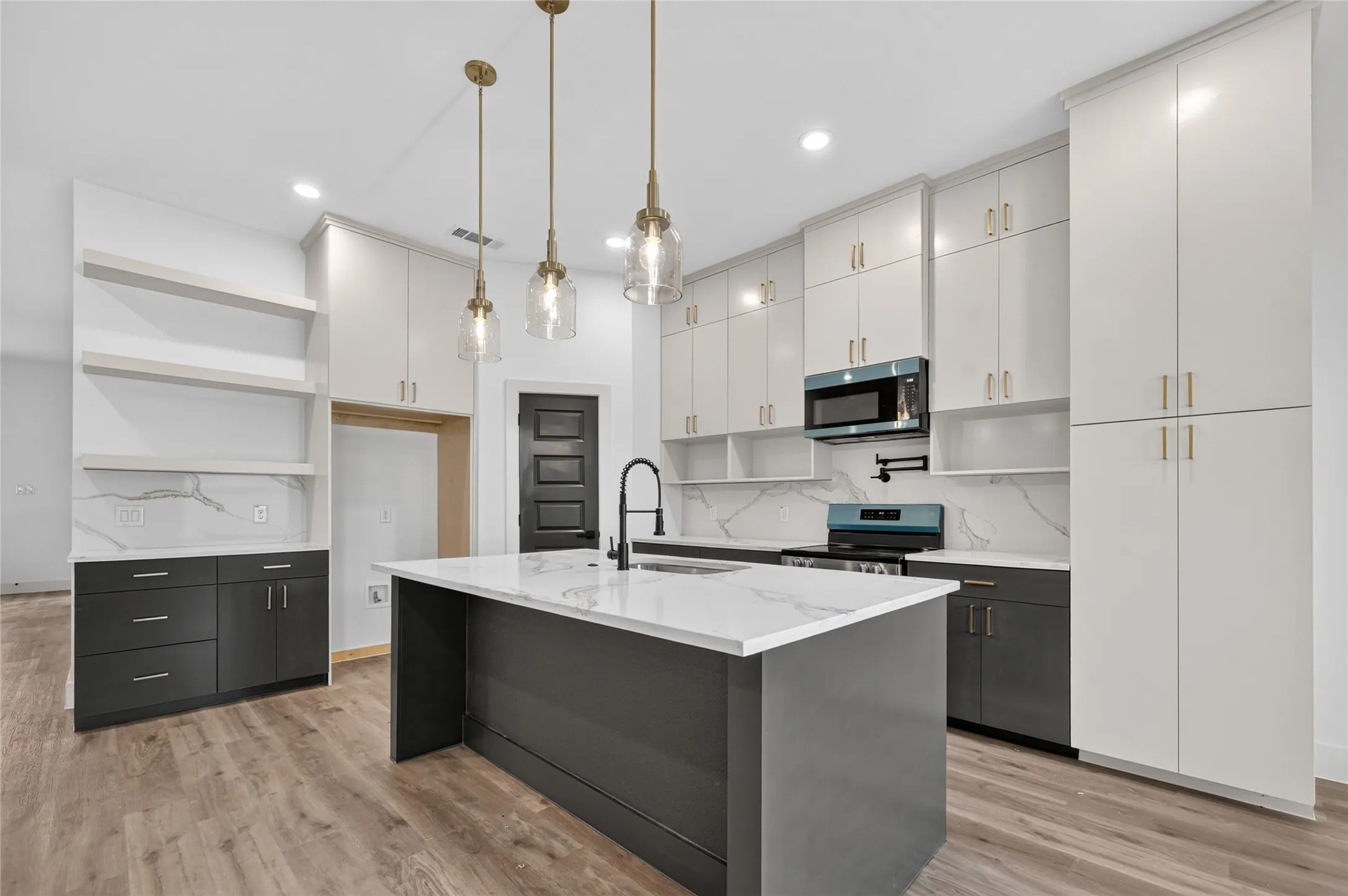 Modern kitchen featuring a central island with a waterfall countertop, contemporary pendant lighting, extensive white cabinetry, high-contrast dark lower cabinets, and wood-finish flooring