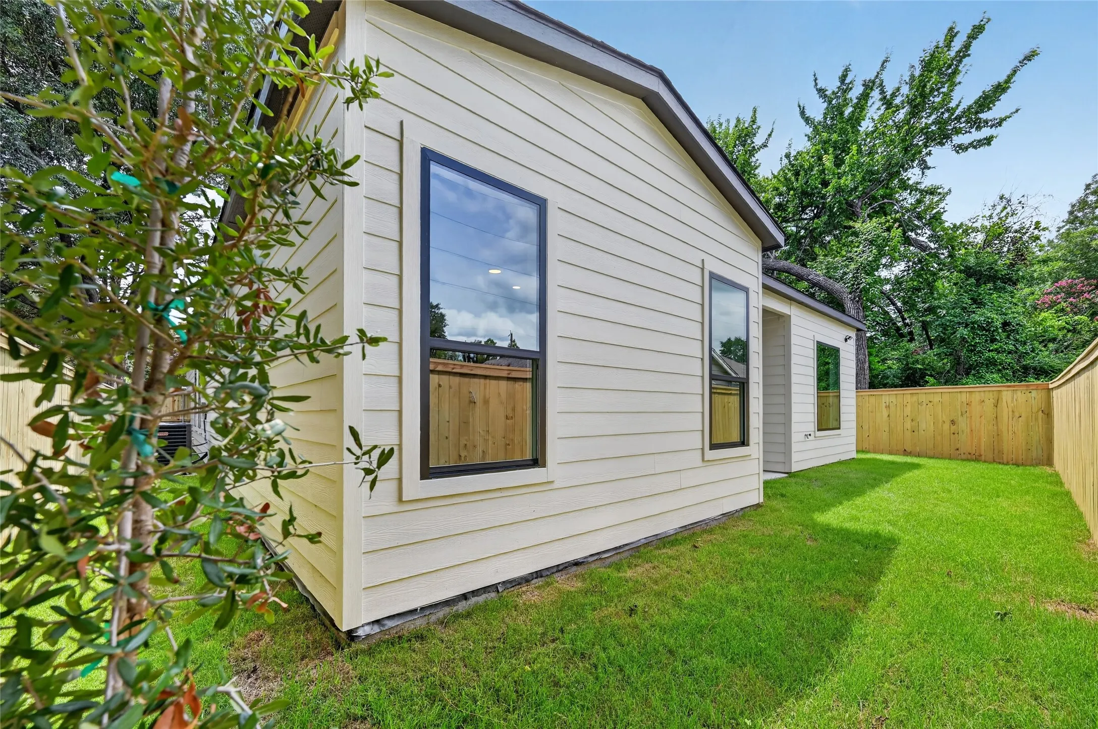 Expansive side yard featuring a manicured lawn, newly installed wood privacy fencing, and a young tree