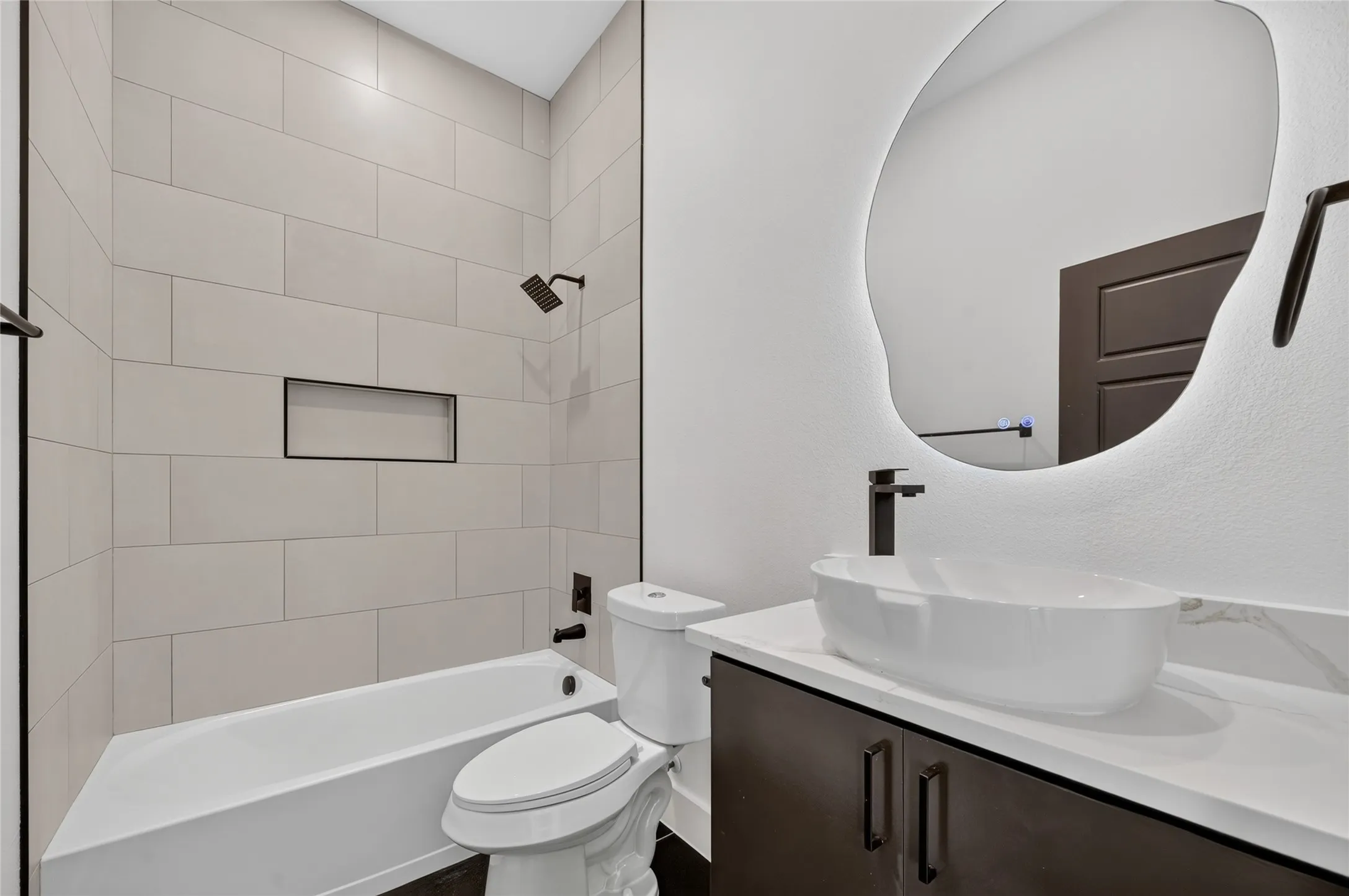 Bathroom featuring a vessel sink, dark wood-finish vanity with stone-look countertop, and an illuminated organic-shaped mirror
